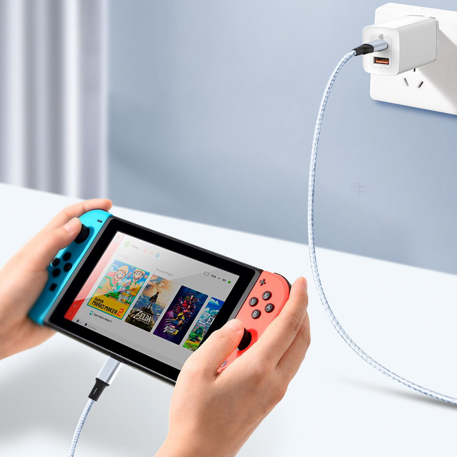 Mani che tengono una Nintendo Switch. È collegata a un cavo di ricarica bianco collegato a una presa a muro.