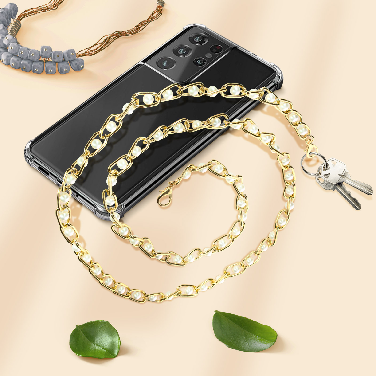 Telefono con collana a catena e chiavi. Foglie posizionate sulla superficie.