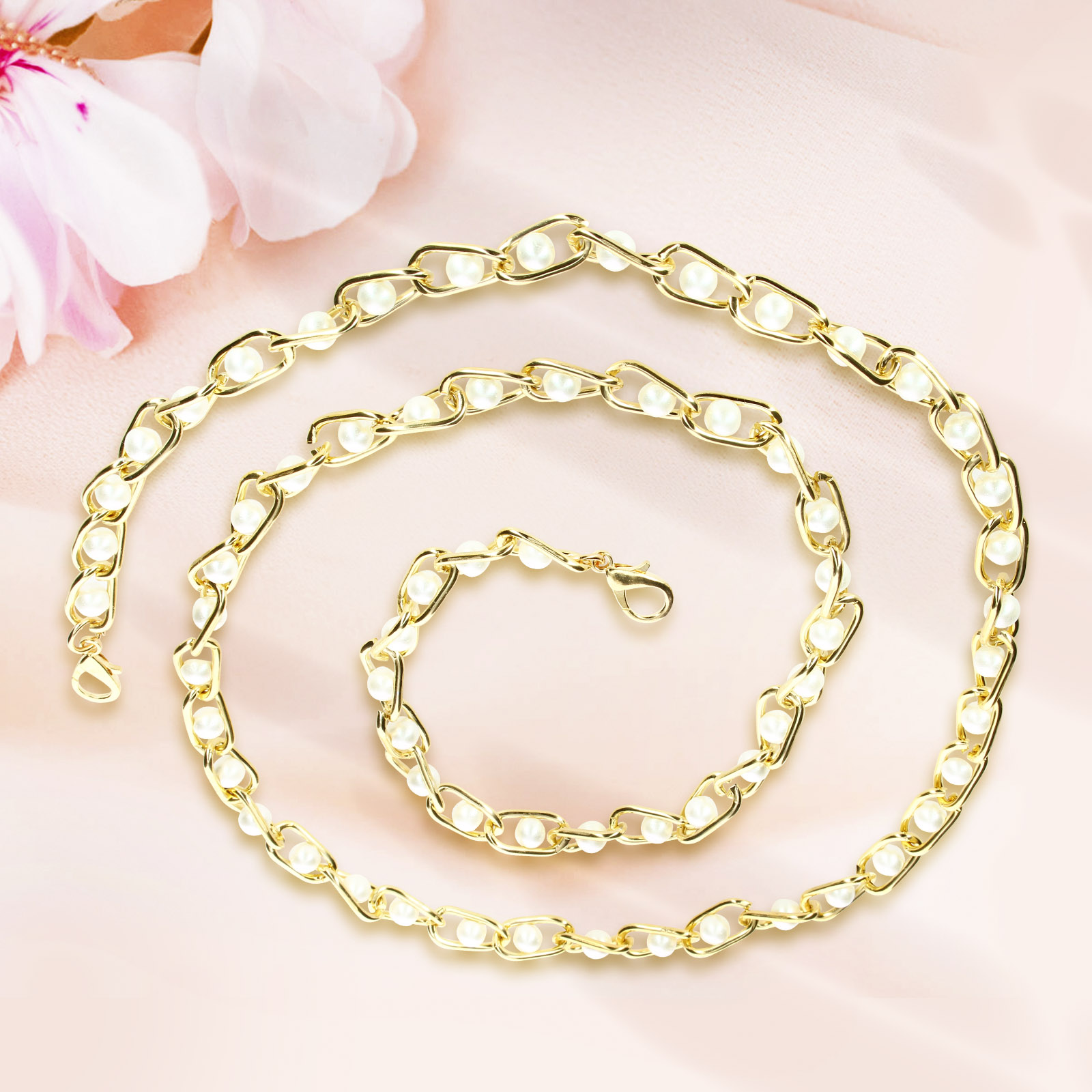 Una collana d'oro con perle bianche. La collana è a forma di spirale su un tessuto rosa.