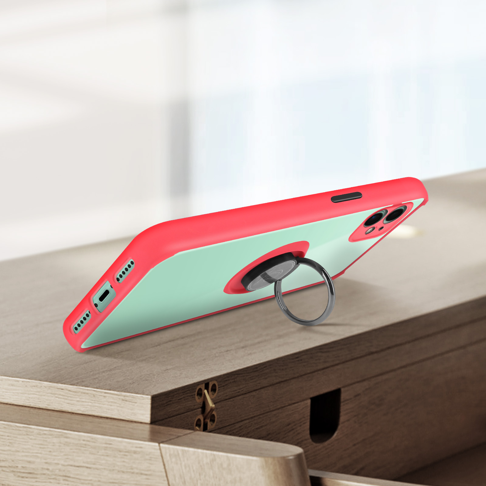 Un étui de téléphone avec un cadre rouge et un dos vert menthe. Un anneau argenté est attaché. L'étui est sur du bois.
