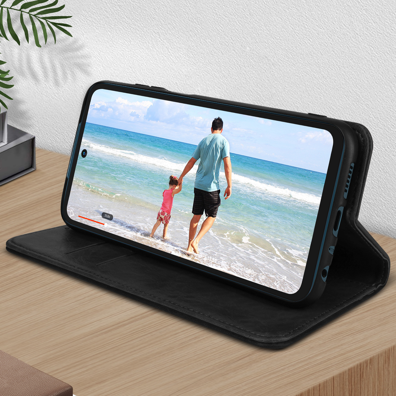 Le téléphone montre une vidéo d'un homme et d'un enfant à la plage. Étui noir sur bois.