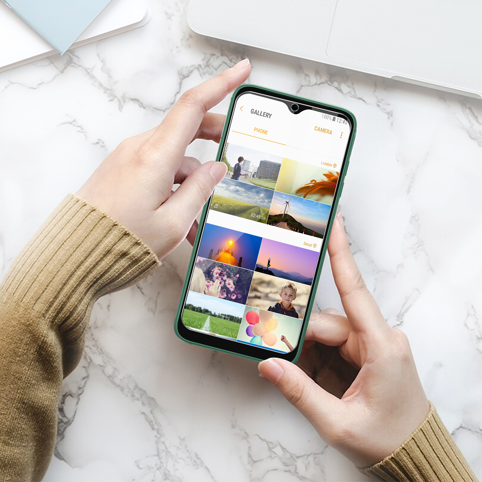 Handen die een telefoon vasthouden met foto's in galerijmodus. De telefoon zit in een groen hoesje.