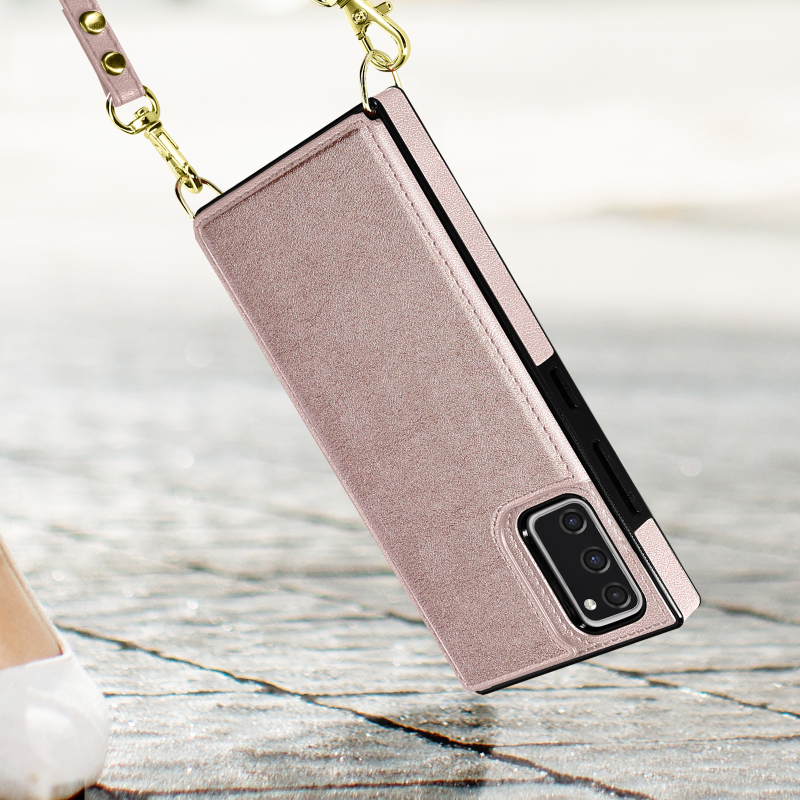 Roze telefoonhoesje met een gouden kettingriem, hangend met een wazige achtergrond.