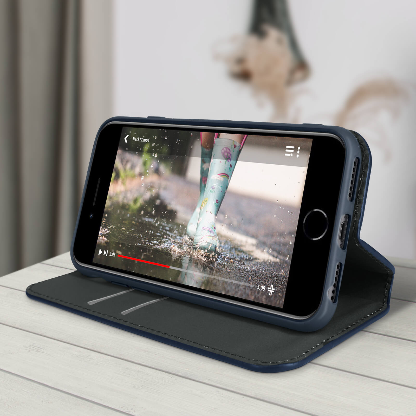 Un téléphone dans un étui lit une vidéo de bottes de pluie éclaboussant dans des flaques. Le téléphone est sur une surface en bois.
