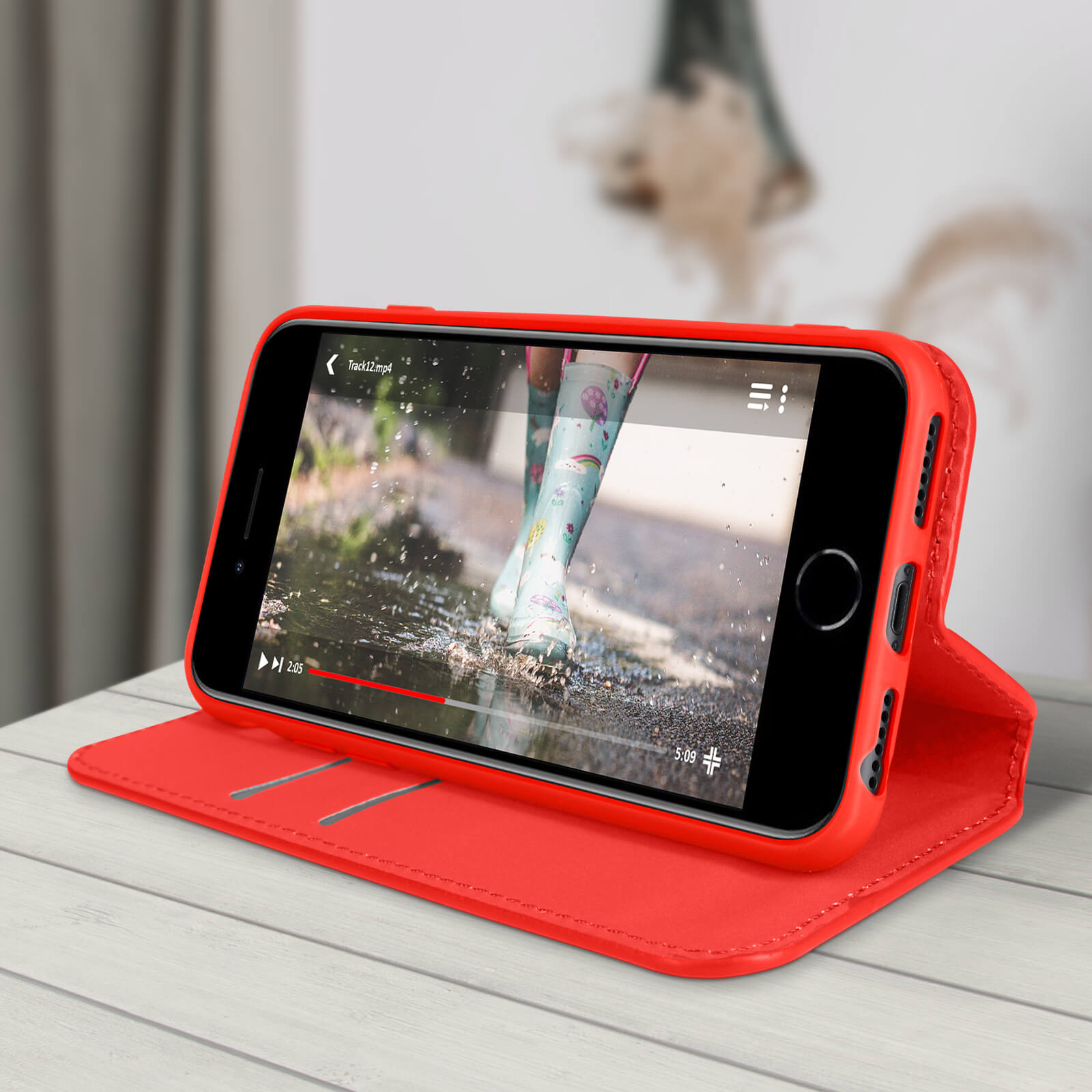 Étui de téléphone rouge avec un téléphone diffusant une vidéo. Le téléphone est sur une surface en bois blanc.