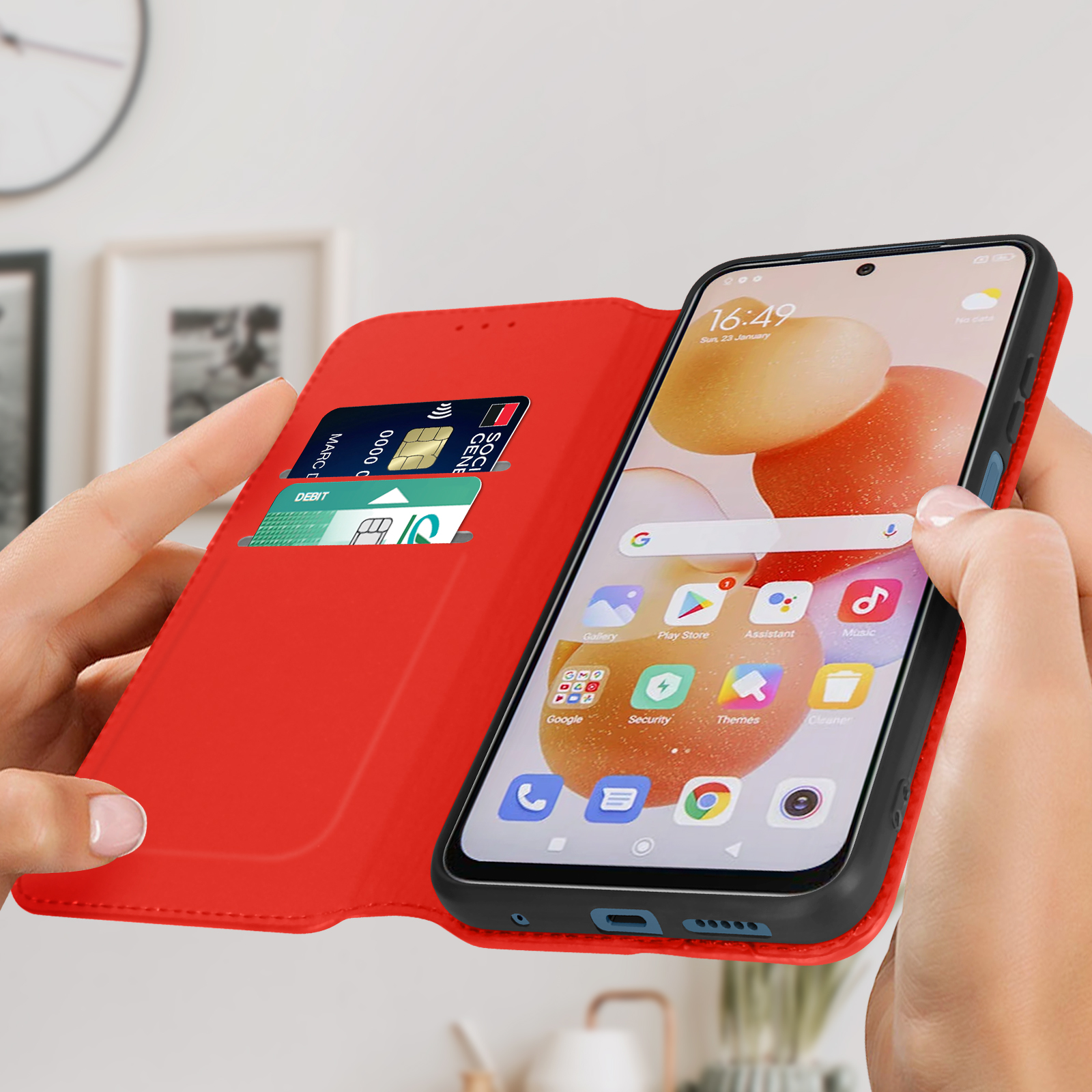 Téléphone ouvert, étui rouge, carte de crédit visible. Mains le tenant.
