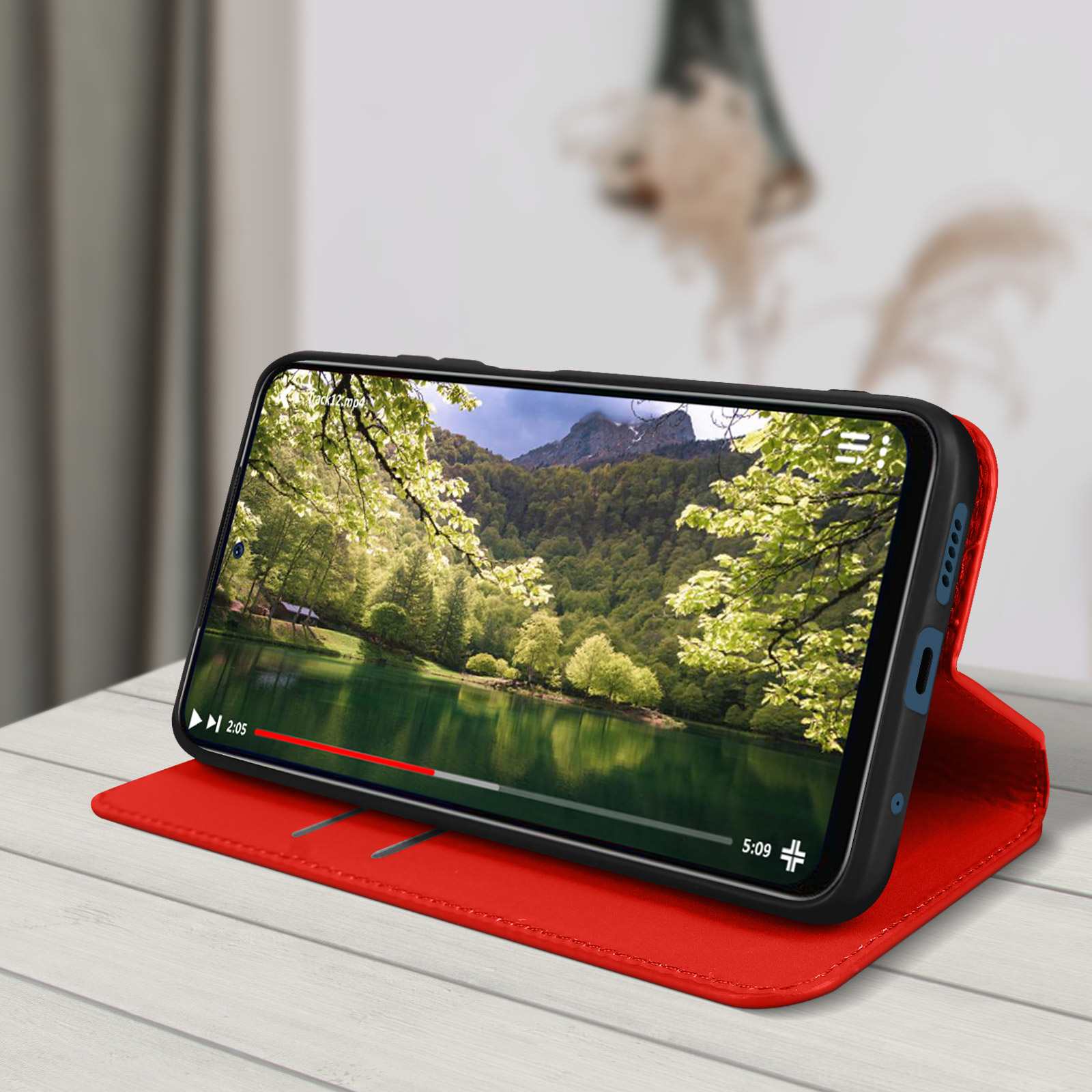 Un téléphone dans un étui rouge affiche une vidéo d'un lac et d'arbres. L'étui est ouvert, sur une table.