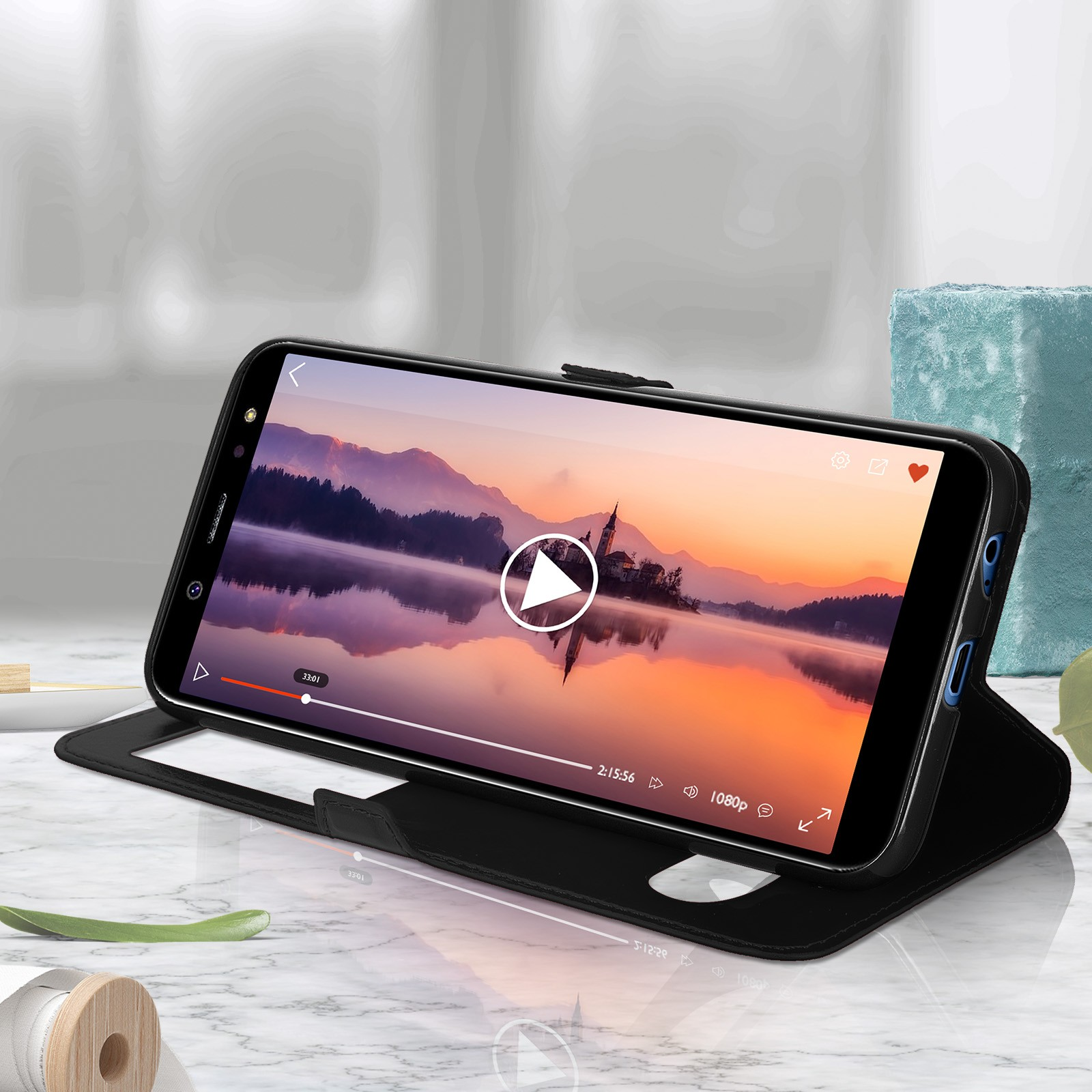 Telefono nero in una custodia di pelle, che riproduce un video. Il telefono è aperto su una superficie bianca.