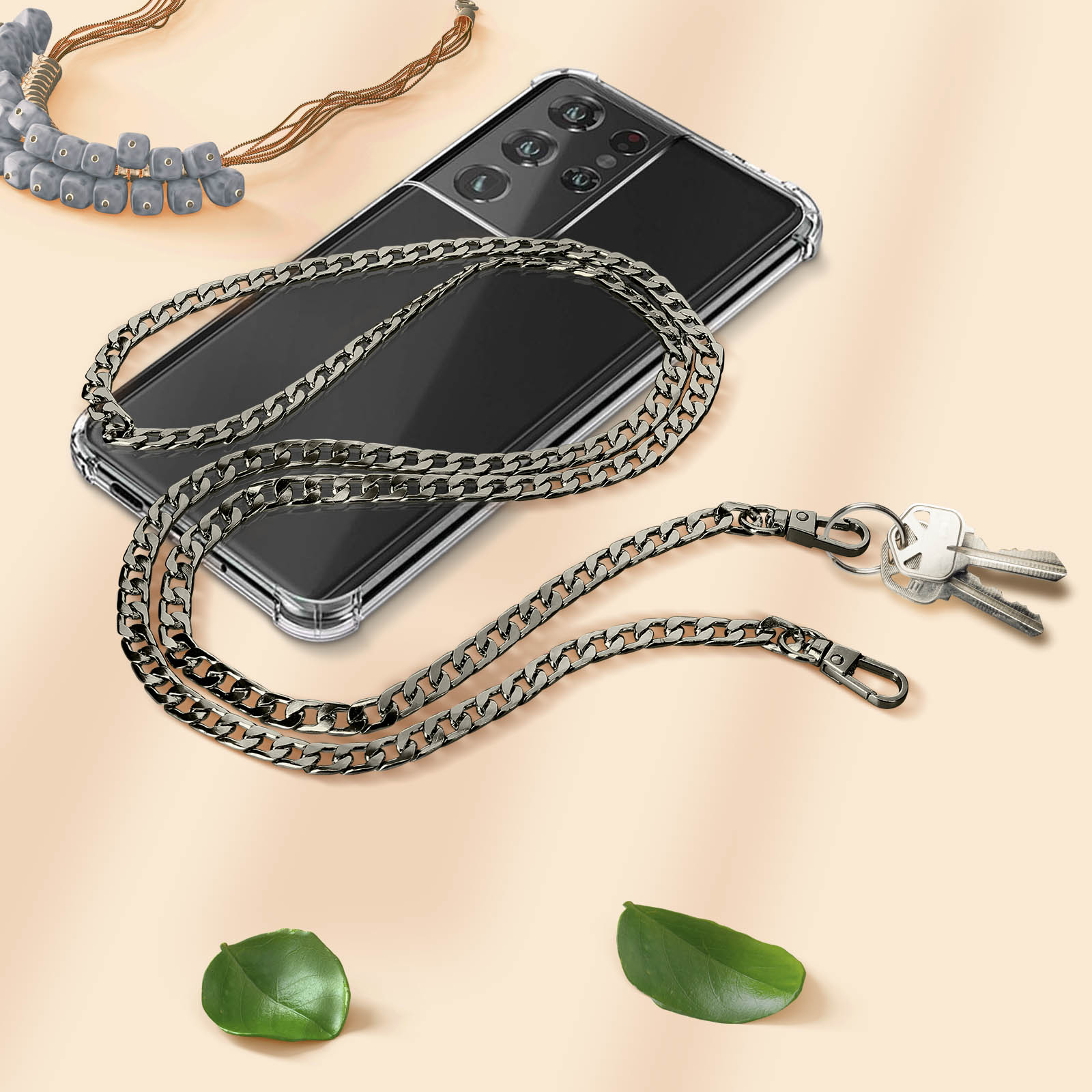 Una cover trasparente per telefono con catena d'argento, chiavi e collana di perline su sfondo beige.