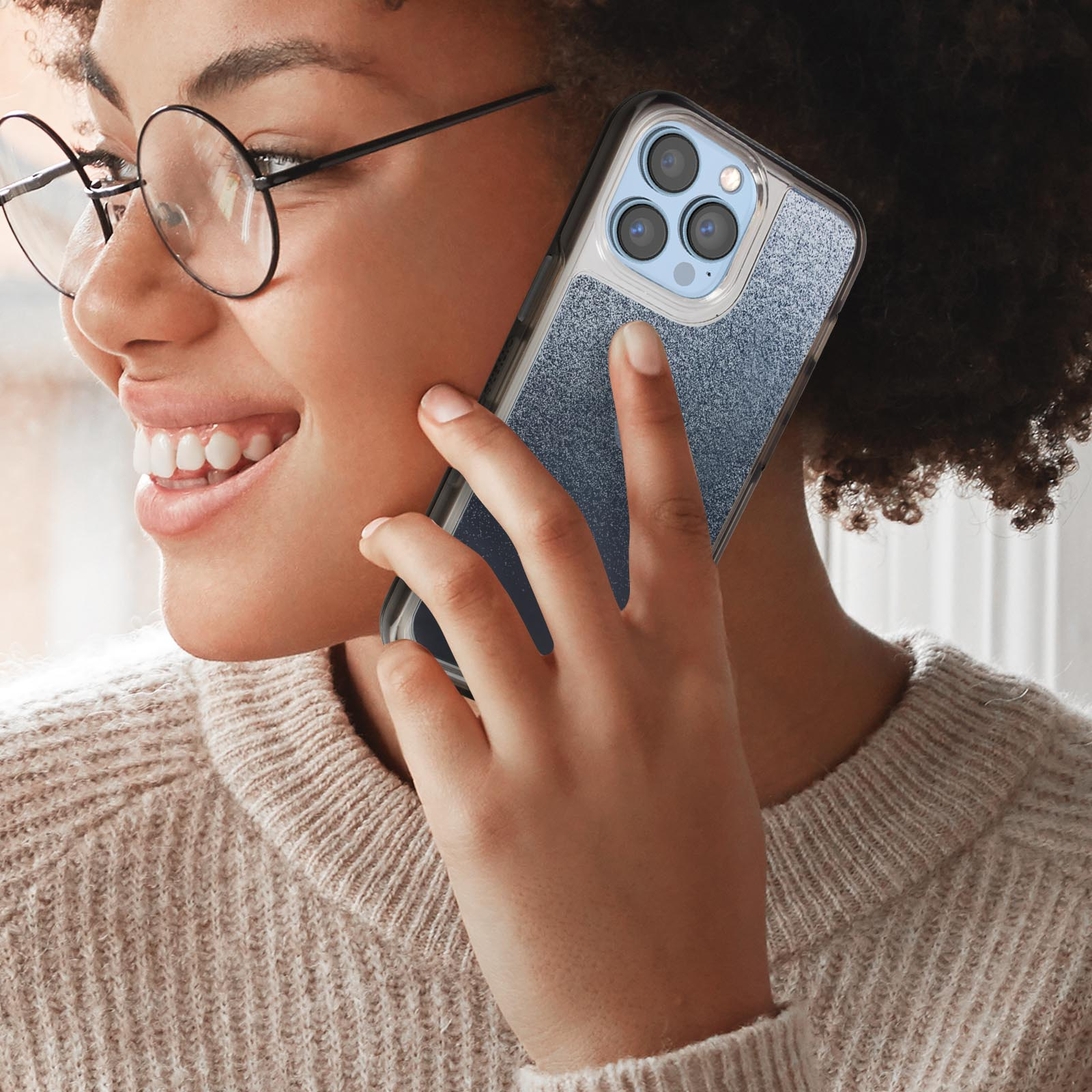 Frau hält Telefon ans Ohr. Das Telefon hat eine blaue Glitzerhülle. Sie lächelt.
