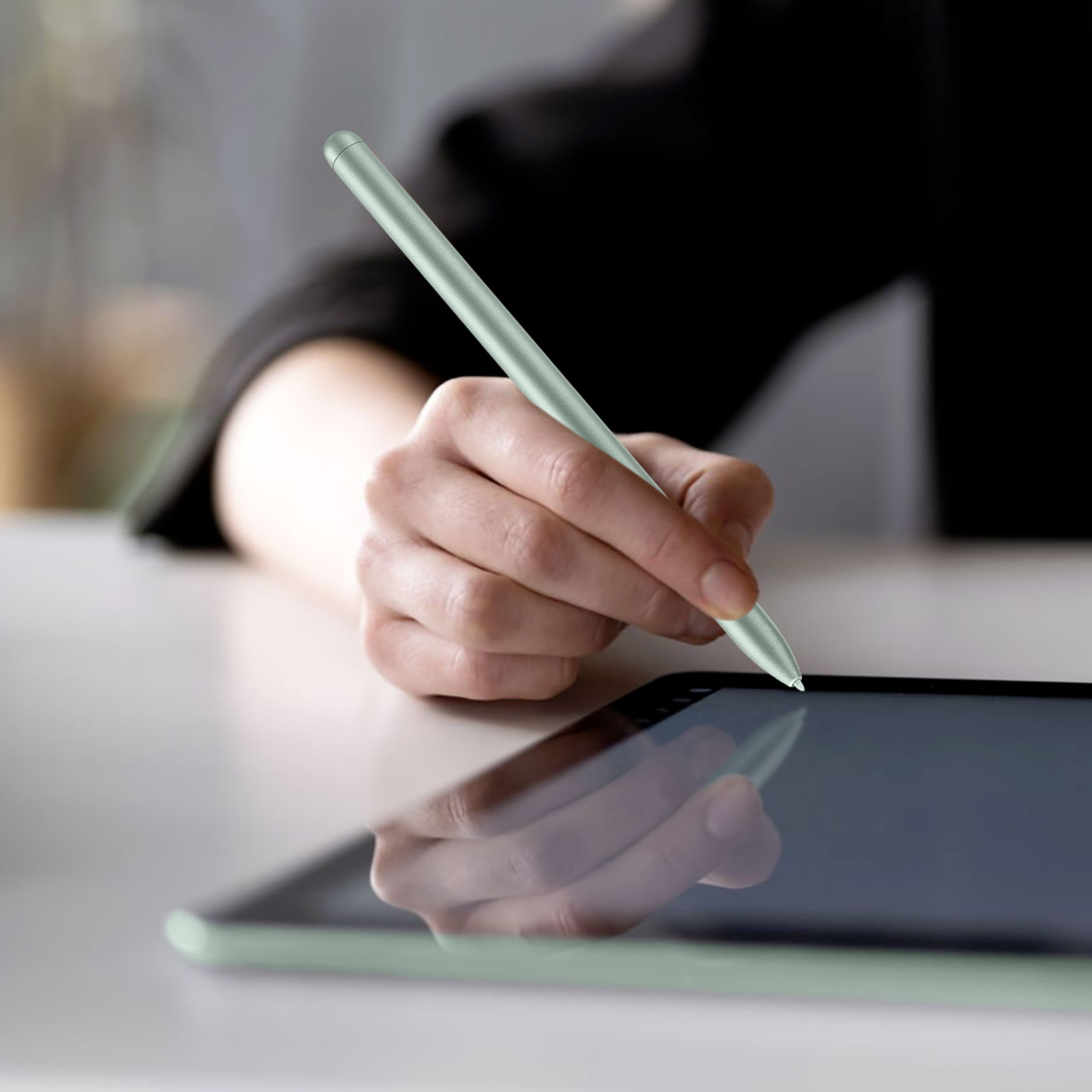 Eine Hand, die einen grünen Stift über einem Tablet hält. Das Tablet liegt auf einem Tisch. Schwarzes Hemd.