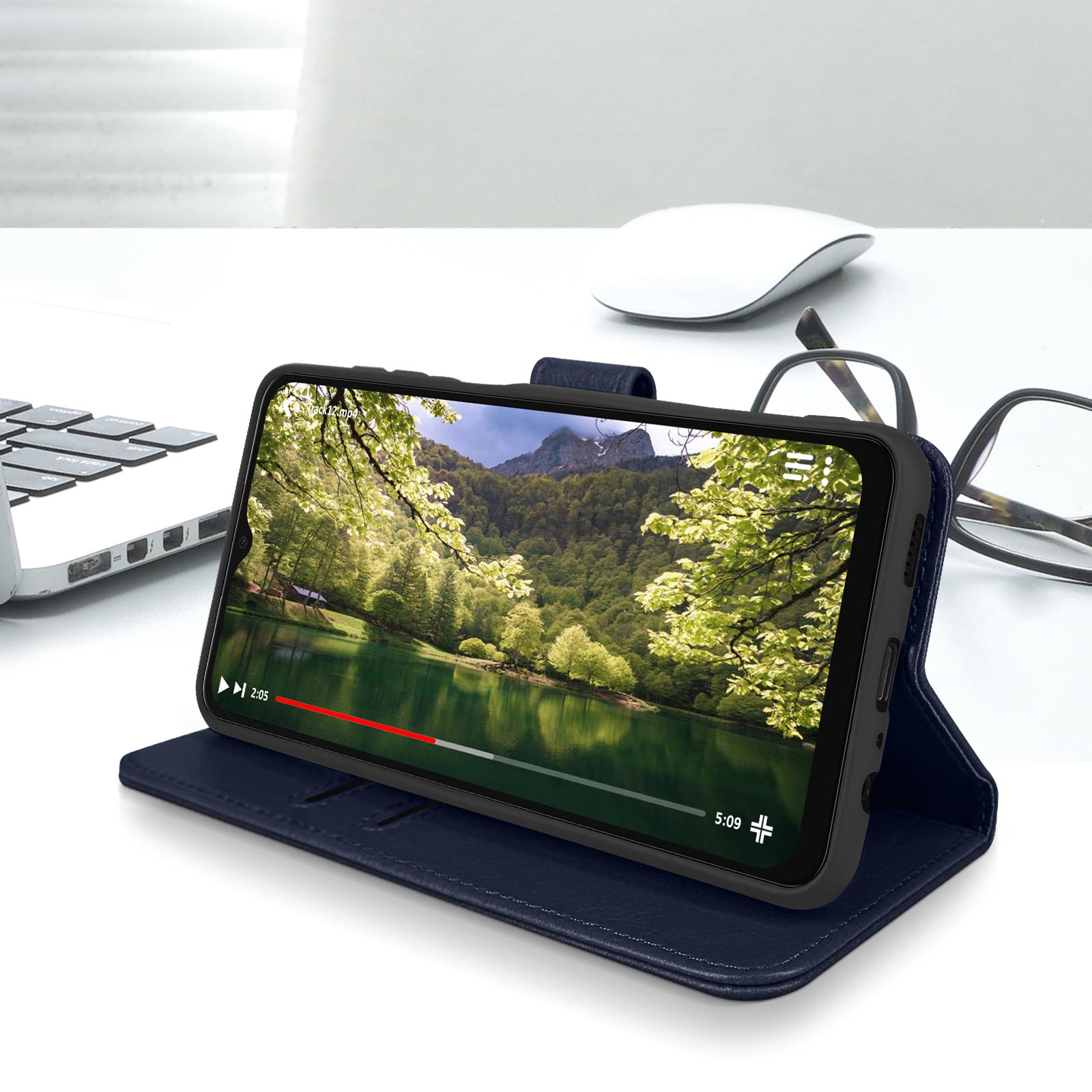 Téléphone avec vidéo d'un lac et de montagnes. Étui ouvert, couvercle bleu. Table blanche, lunettes et souris.