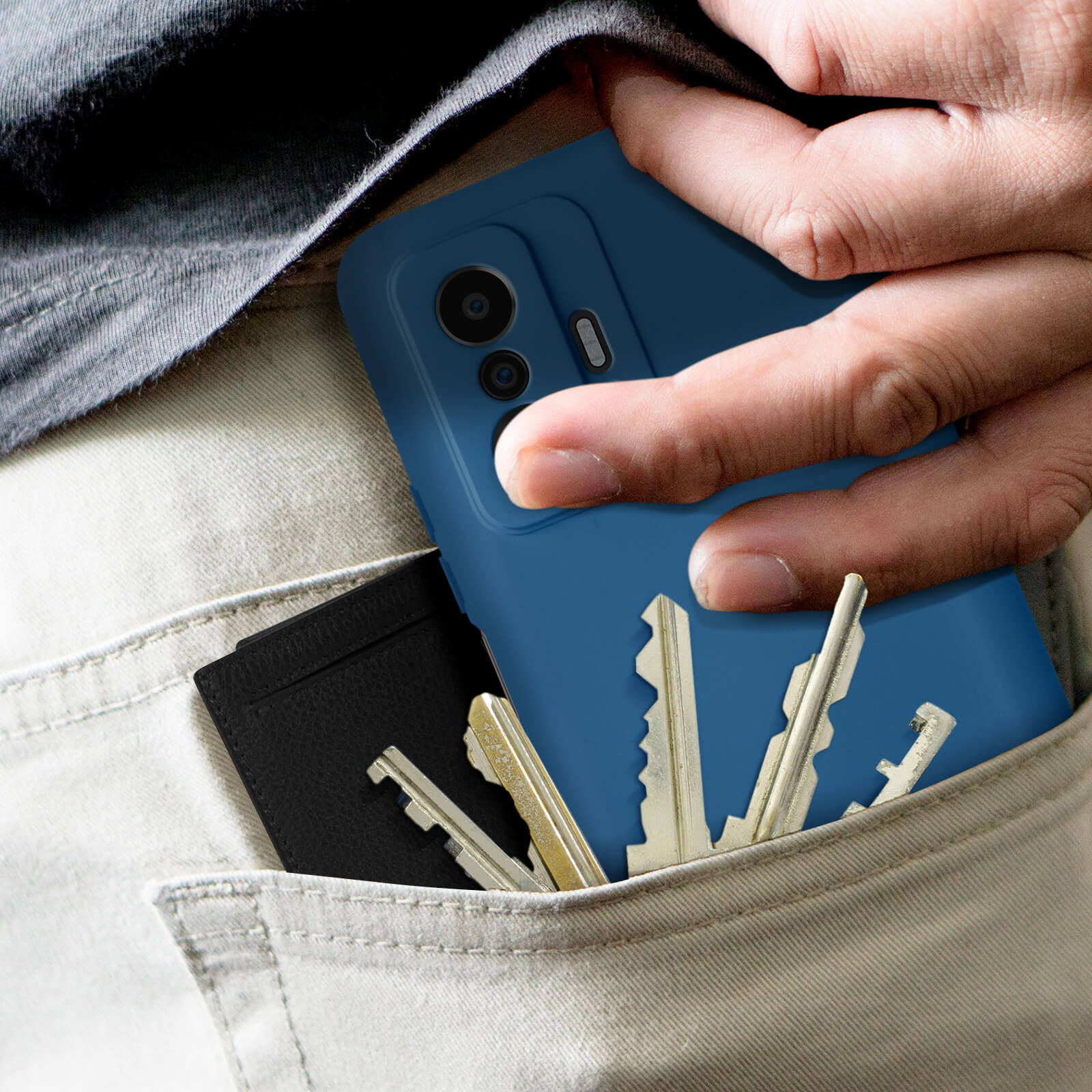 Una mano che mette un telefono blu in tasca con chiavi e un portafoglio nero.