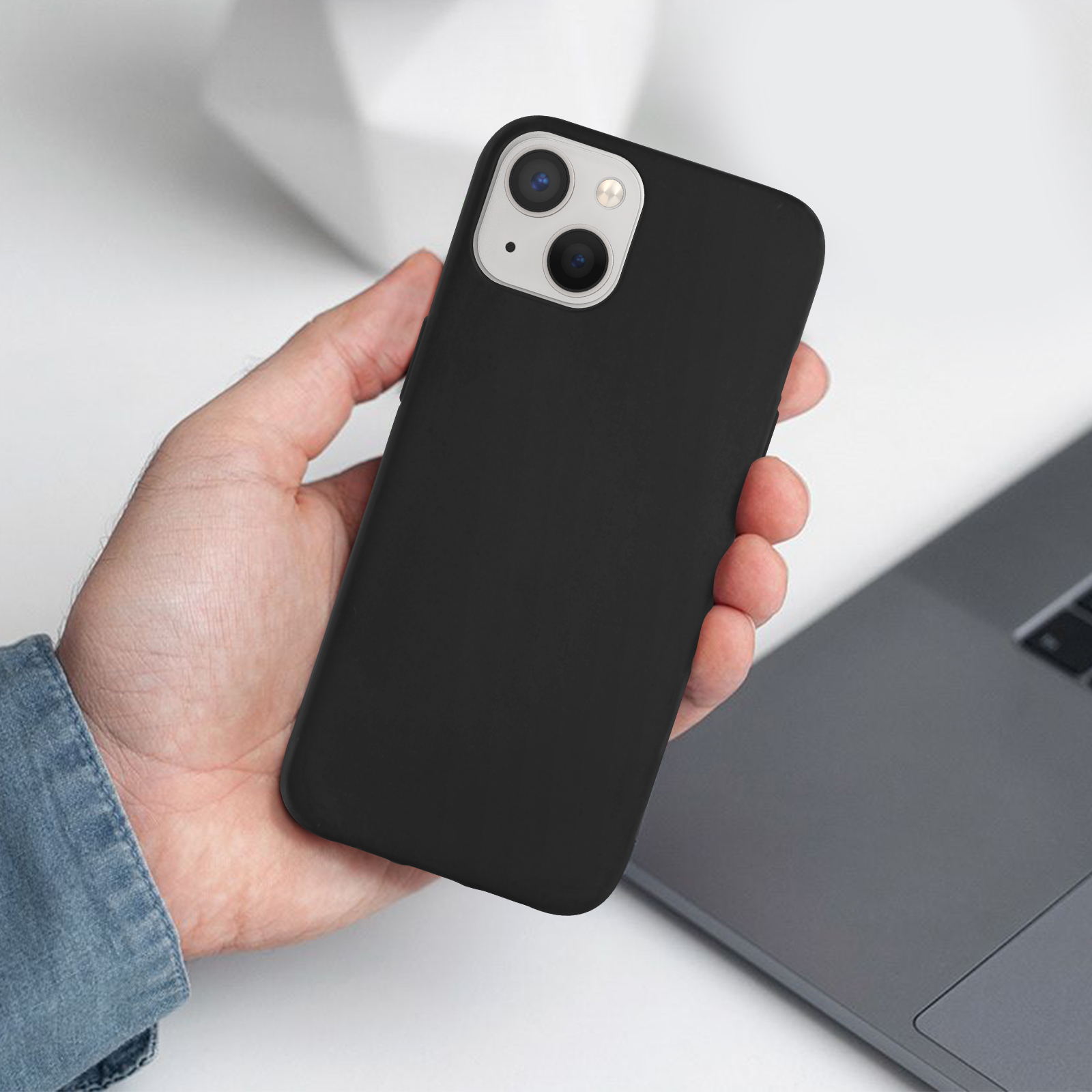 Mano che tiene un telefono nero con custodia nera. Il telefono è sopra un laptop.