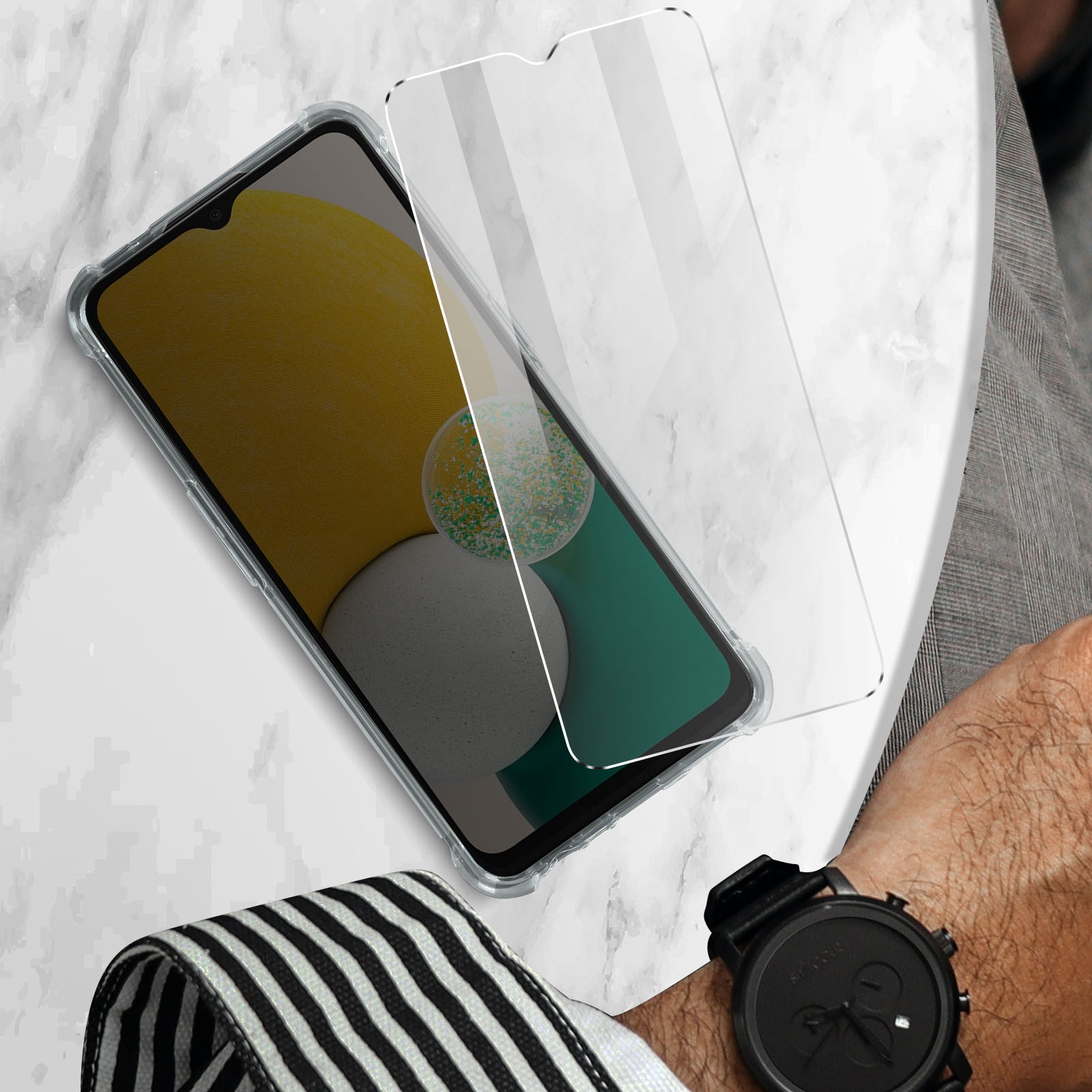 Telefono con schermo giallo e protezione schermo in vetro su marmo, con orologio e camicia.