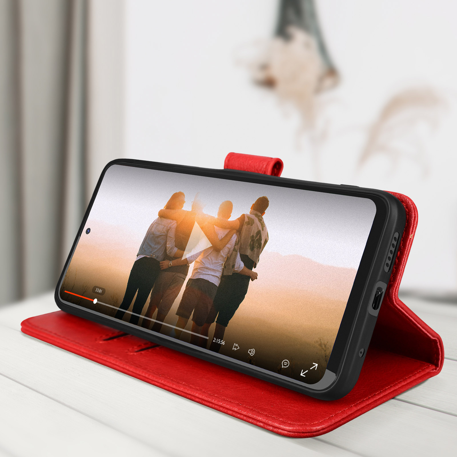 Una custodia rossa per telefono con un telefono che riproduce un video. Persone nel video. Un tavolo bianco.