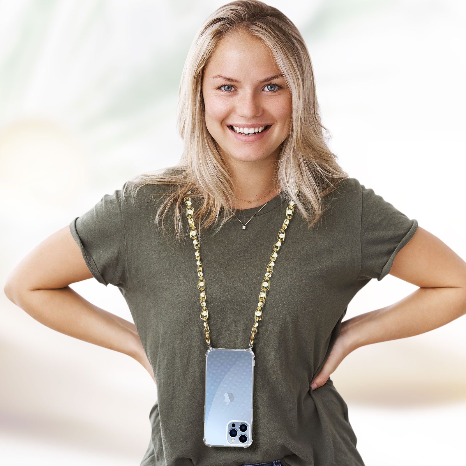 Donna con collana per custodia del telefono. Telefono in custodia trasparente con catena dorata. Sorridente, sfondo chiaro.