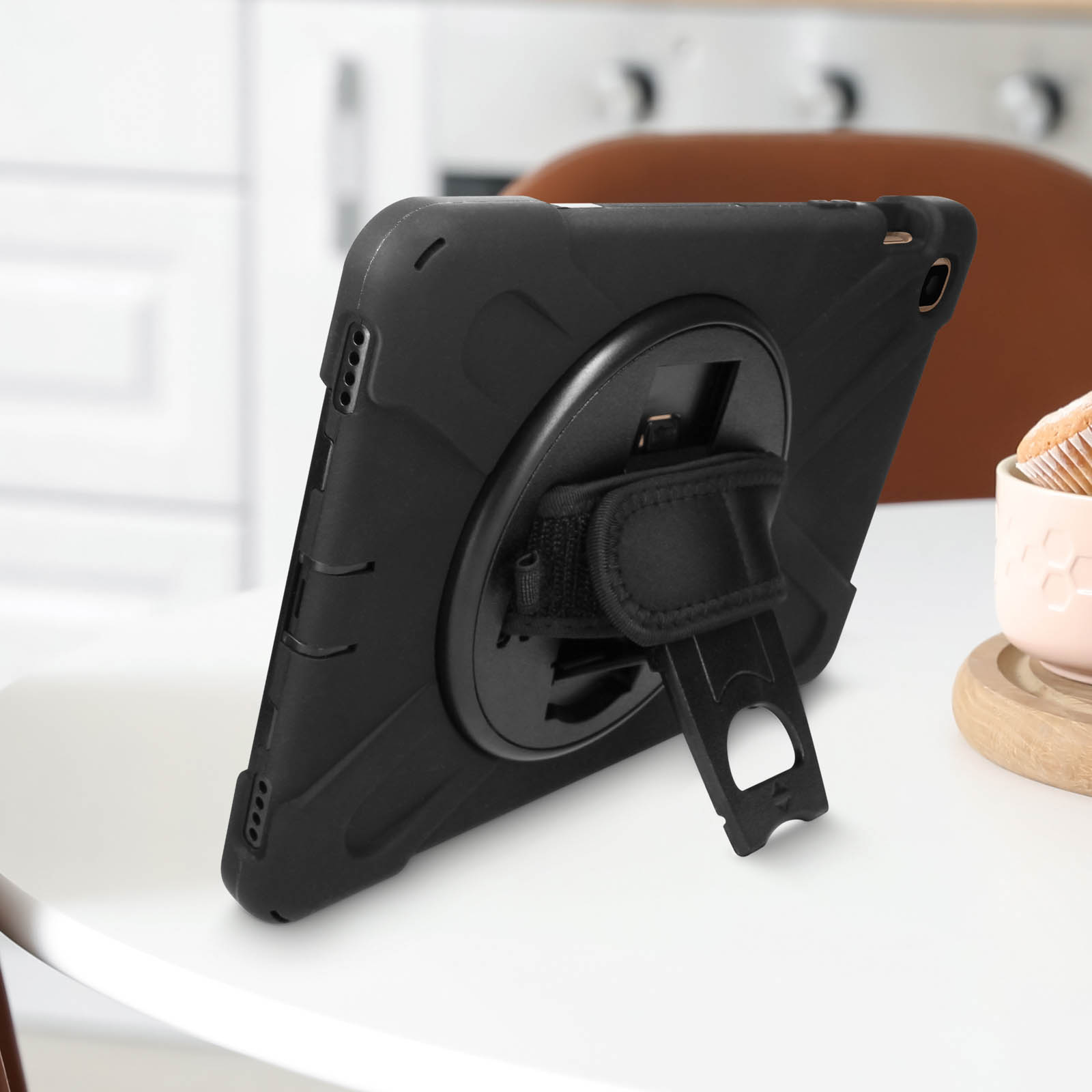 Schwarze Tablet-Hülle mit Riemen und Ständer auf einem weißen Tisch. Küche im Hintergrund.