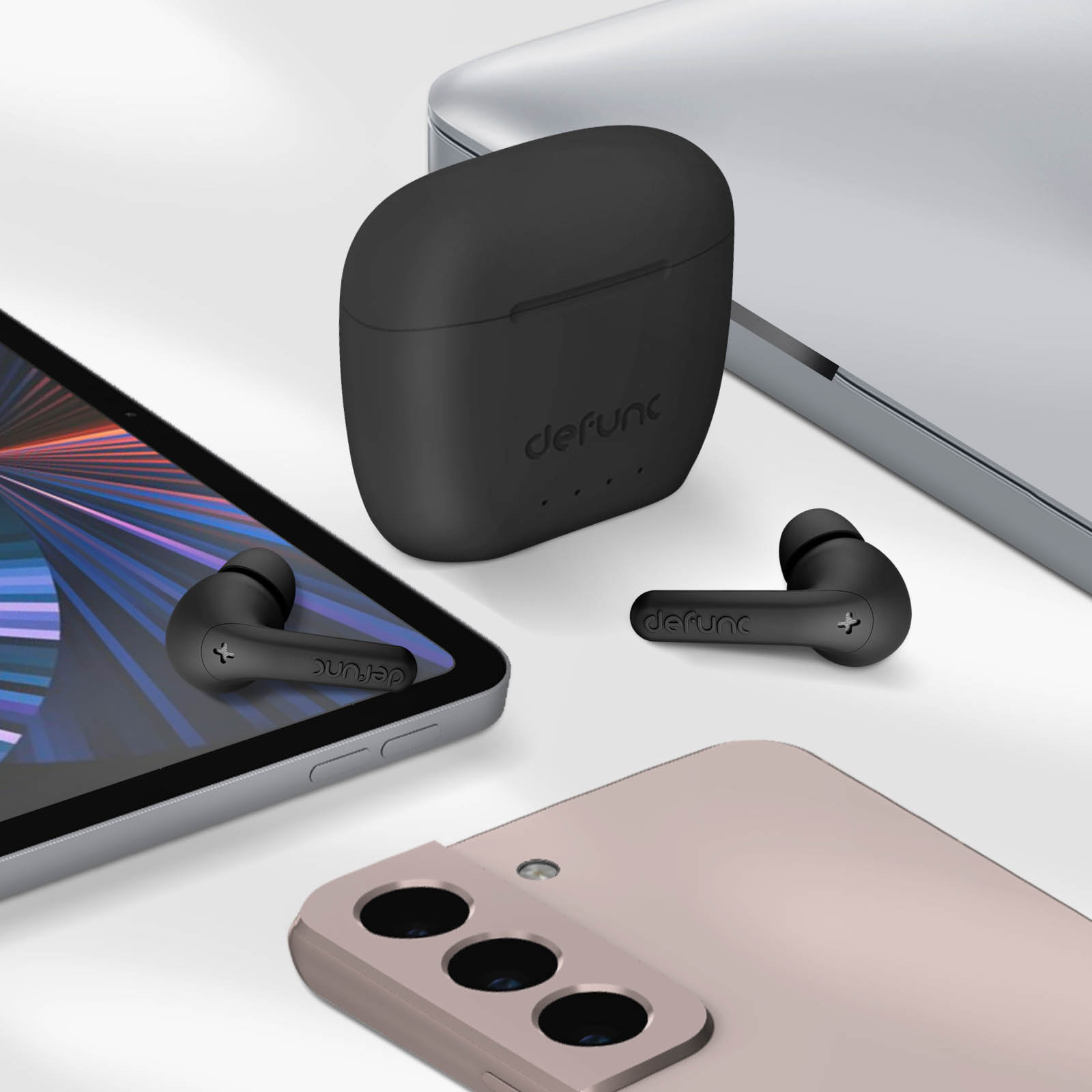 Słuchawki, etui ładujące, dwa telefony i tablet na białej powierzchni.