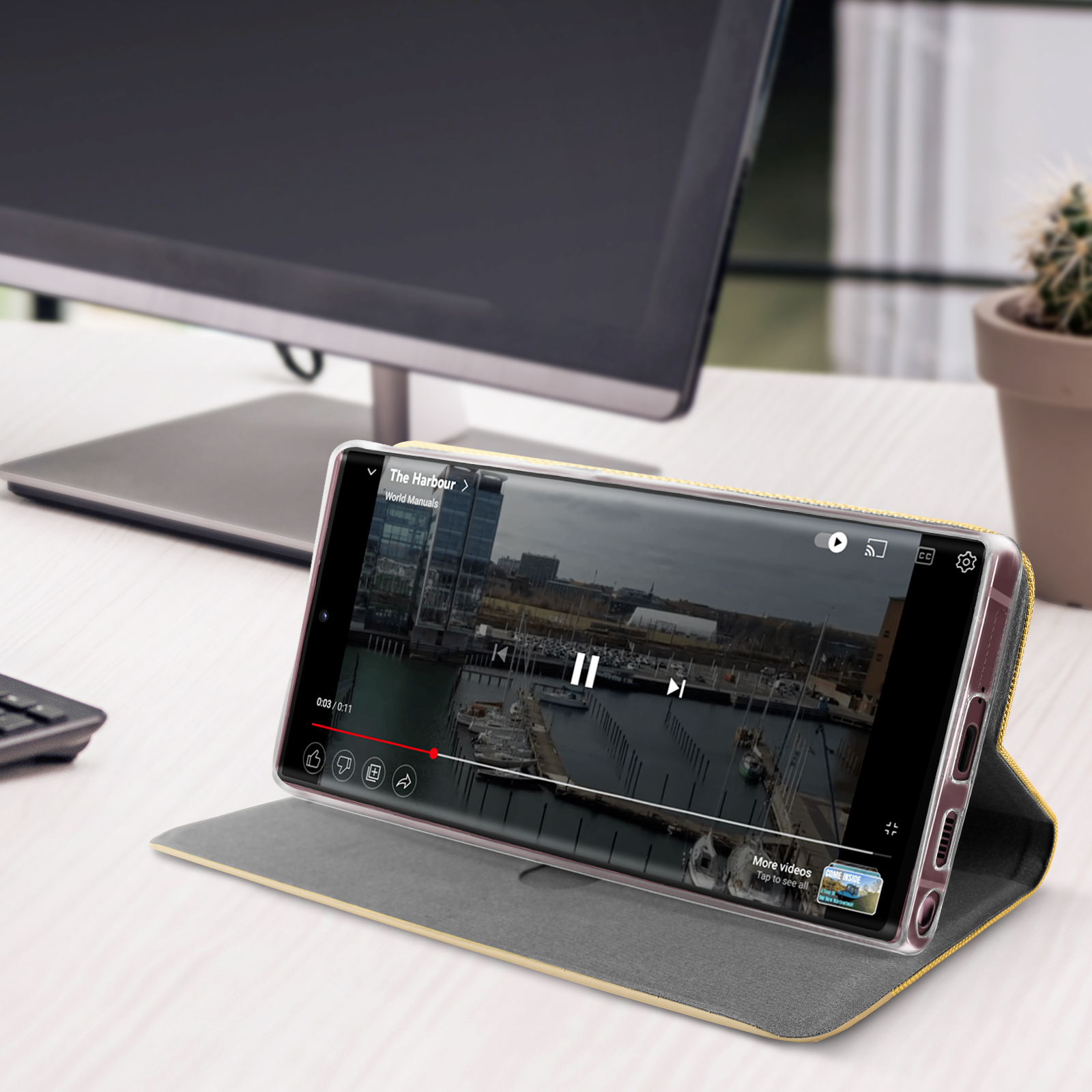 Un teléfono muestra un video de un puerto. El teléfono está en una funda amarilla y gris y está sobre una mesa.