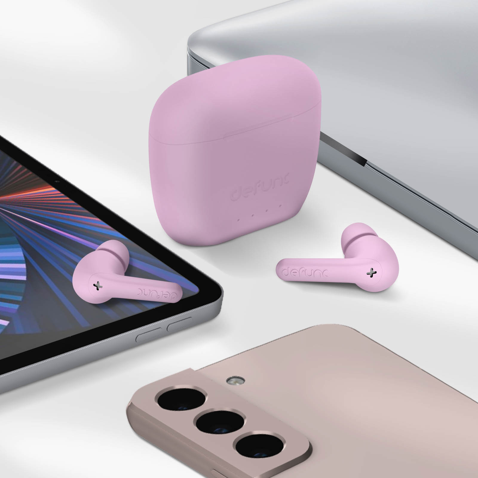 Auricolari e custodia di ricarica in rosa, insieme a un tablet e un telefono. Tutto su una superficie bianca.