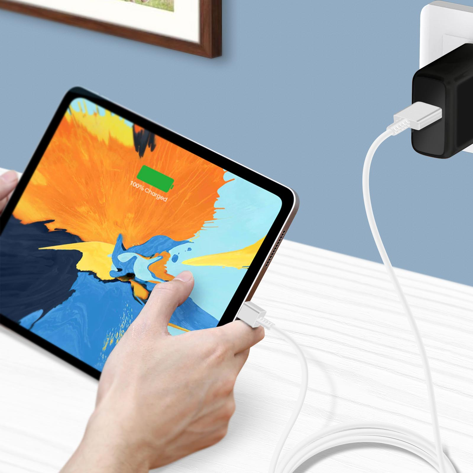 Osoba trzymająca tablet ładujący się białym kablem z czarnym adapterem.