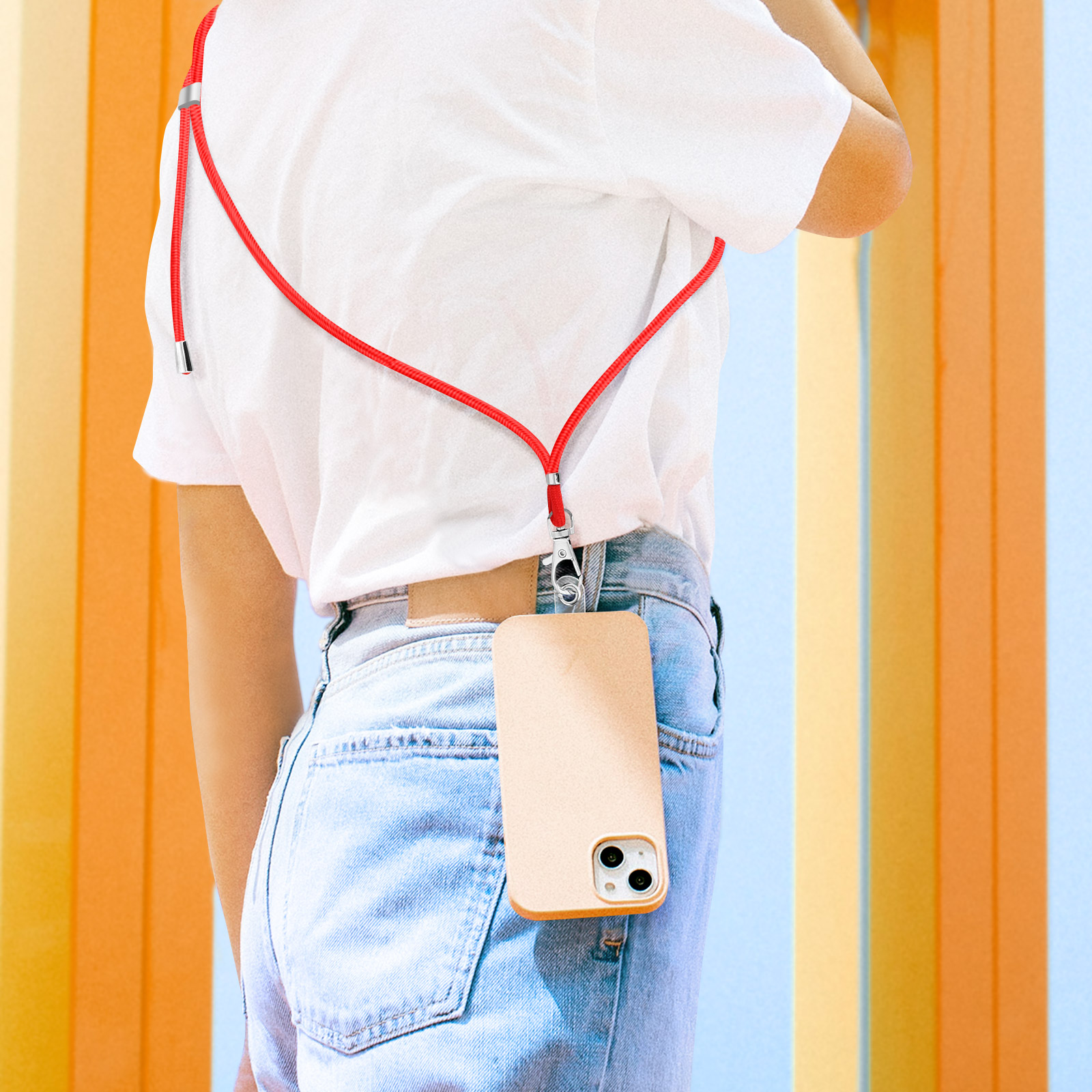 Una persona indossa jeans e una maglietta bianca con un cordino rosso attaccato a un telefono.