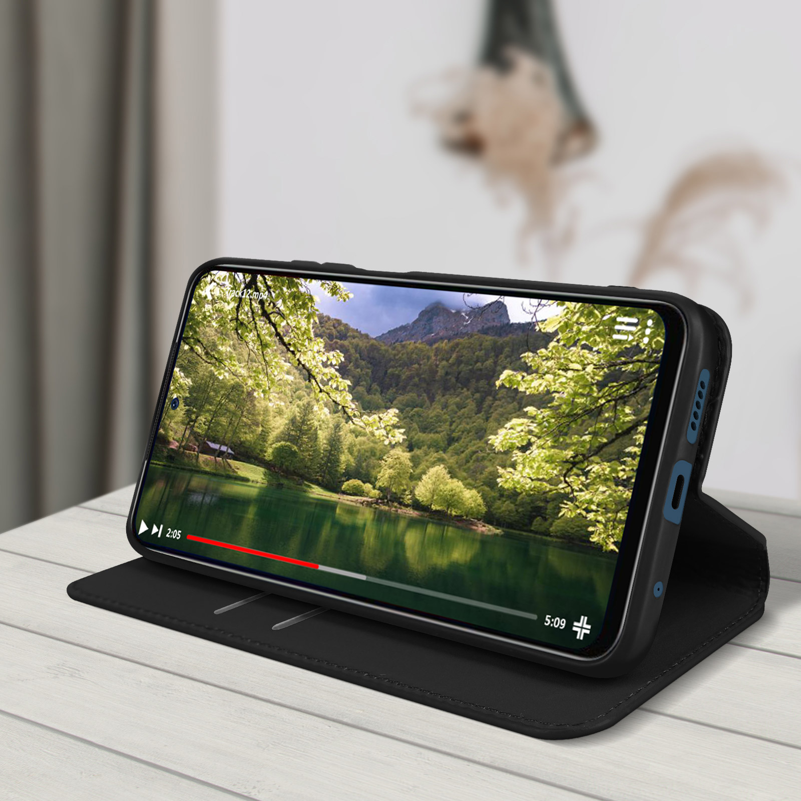 Un téléphone dans un étui noir affiche une vidéo d'un lac et d'arbres. L'étui est ouvert, sur une table.
