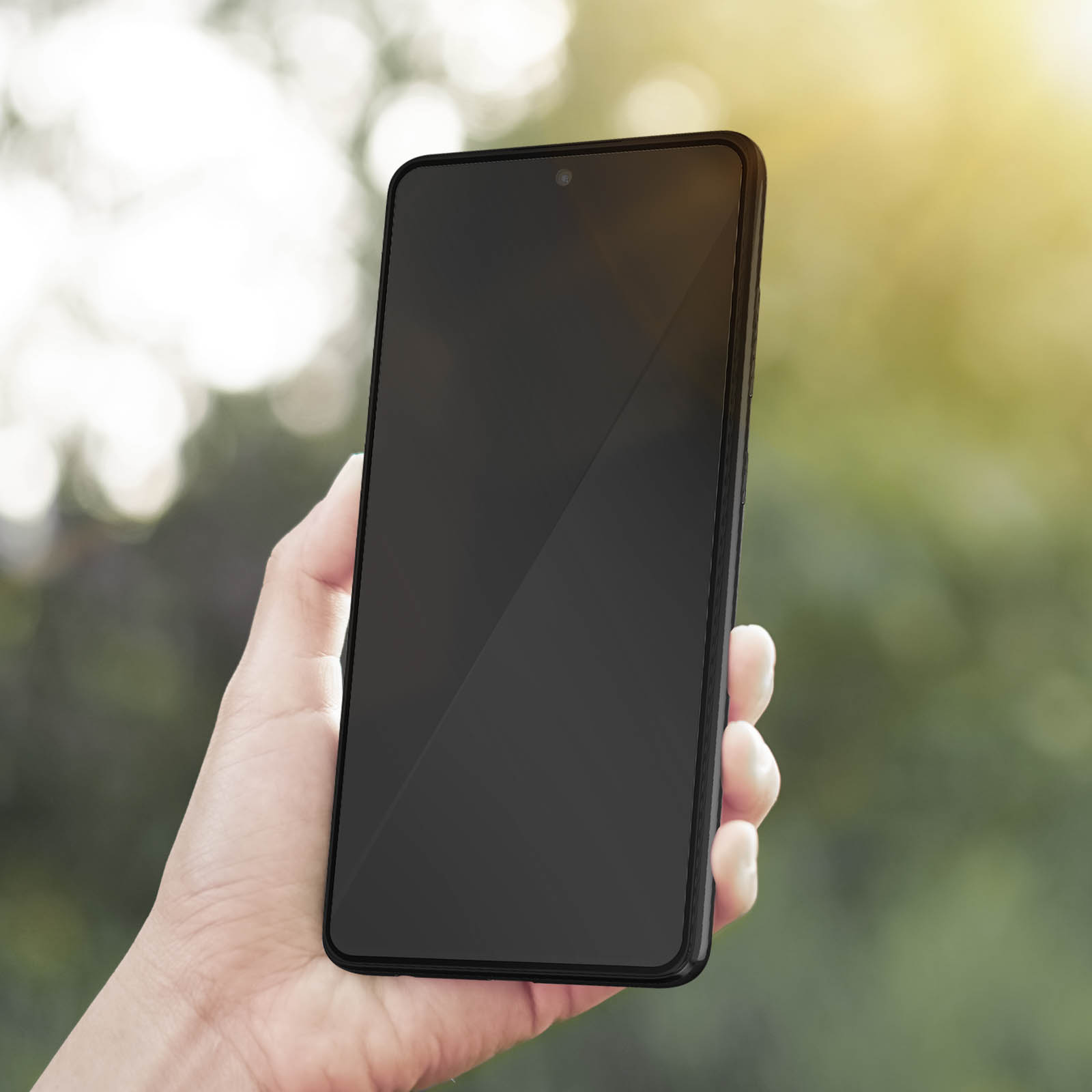 Mano che tiene un telefono nero con schermo nero, sfondo verde sfocato, luce solare.