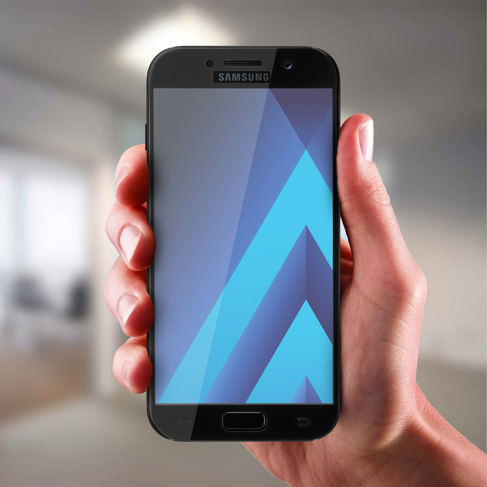 Una mano tiene un telefono Samsung nero. Lo schermo mostra forme geometriche blu e azzurre. Sfondo sfocato.