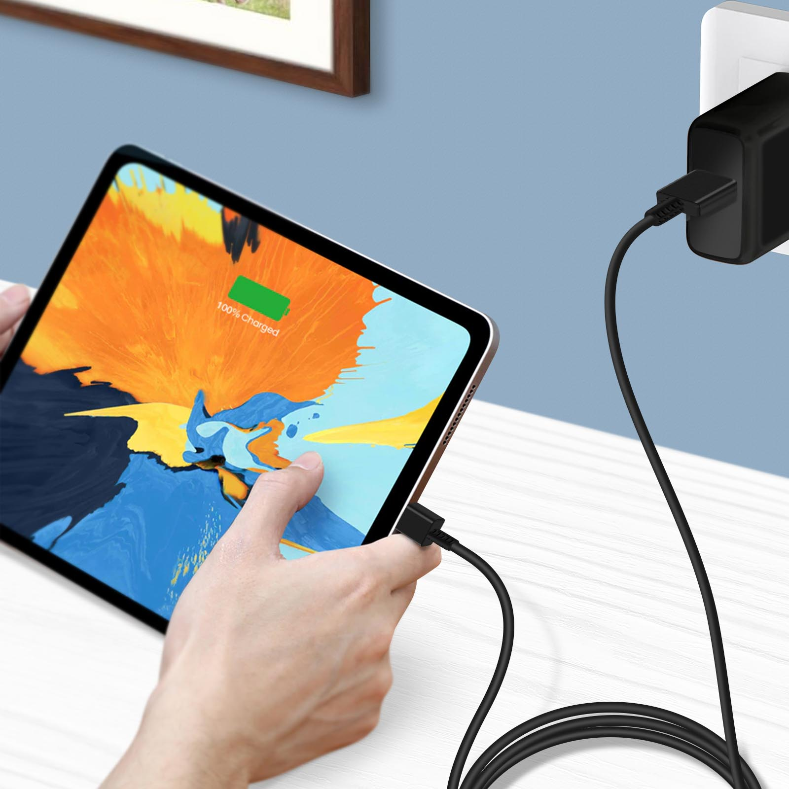 Eine Hand steckt ein Ladekabel in ein Tablet. Ein Wandladegerät ist sichtbar.