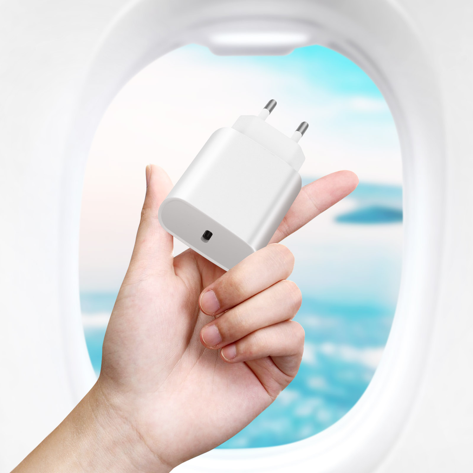 Caricabatterie bianco per telefono tenuto in mano. Lo sfondo mostra un finestrino dell'aereo.