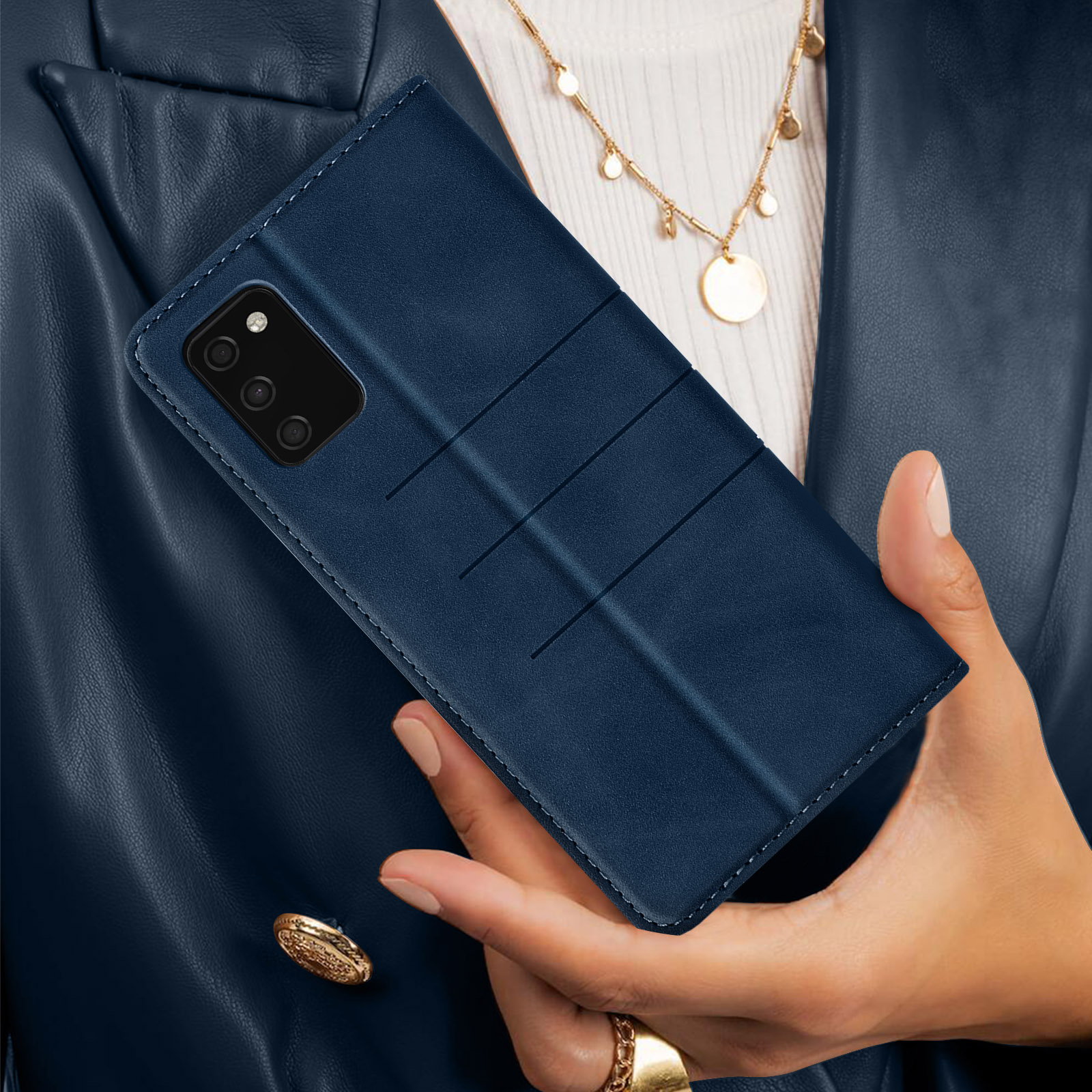 Le mani di una donna che tengono una custodia blu per telefono chiusa. Una collana e una giacca blu sullo sfondo.