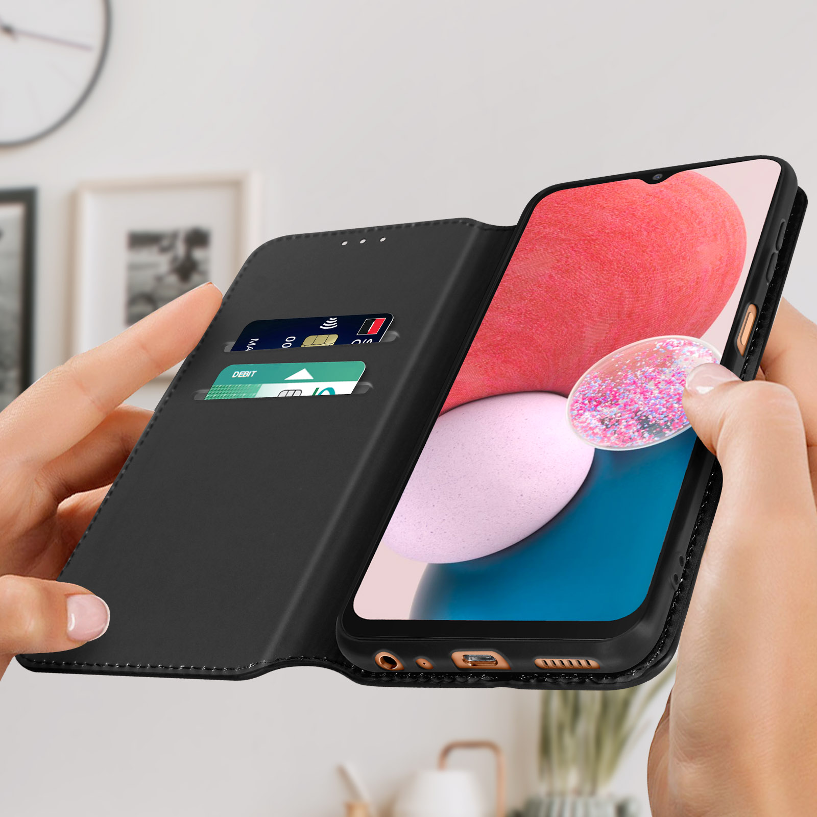 Een zwarte telefoonhoes met een telefoon die roze en blauwe beelden toont, vastgehouden door handen met kaarten erin.