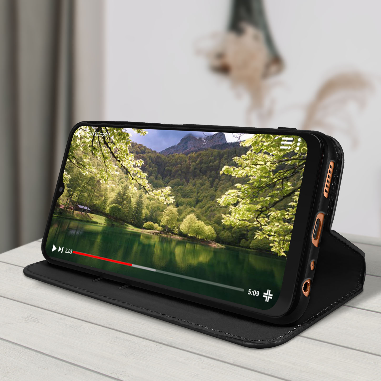 Telefoon in zwarte hoes speelt video af op een tafel. Natuurscène op het scherm.