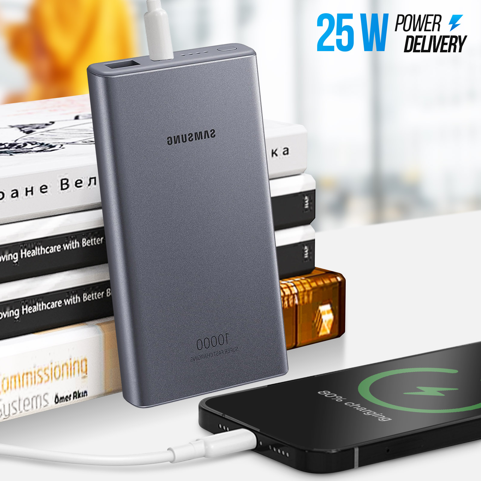 Une batterie externe grise chargeant un téléphone noir. Des livres en arrière-plan.