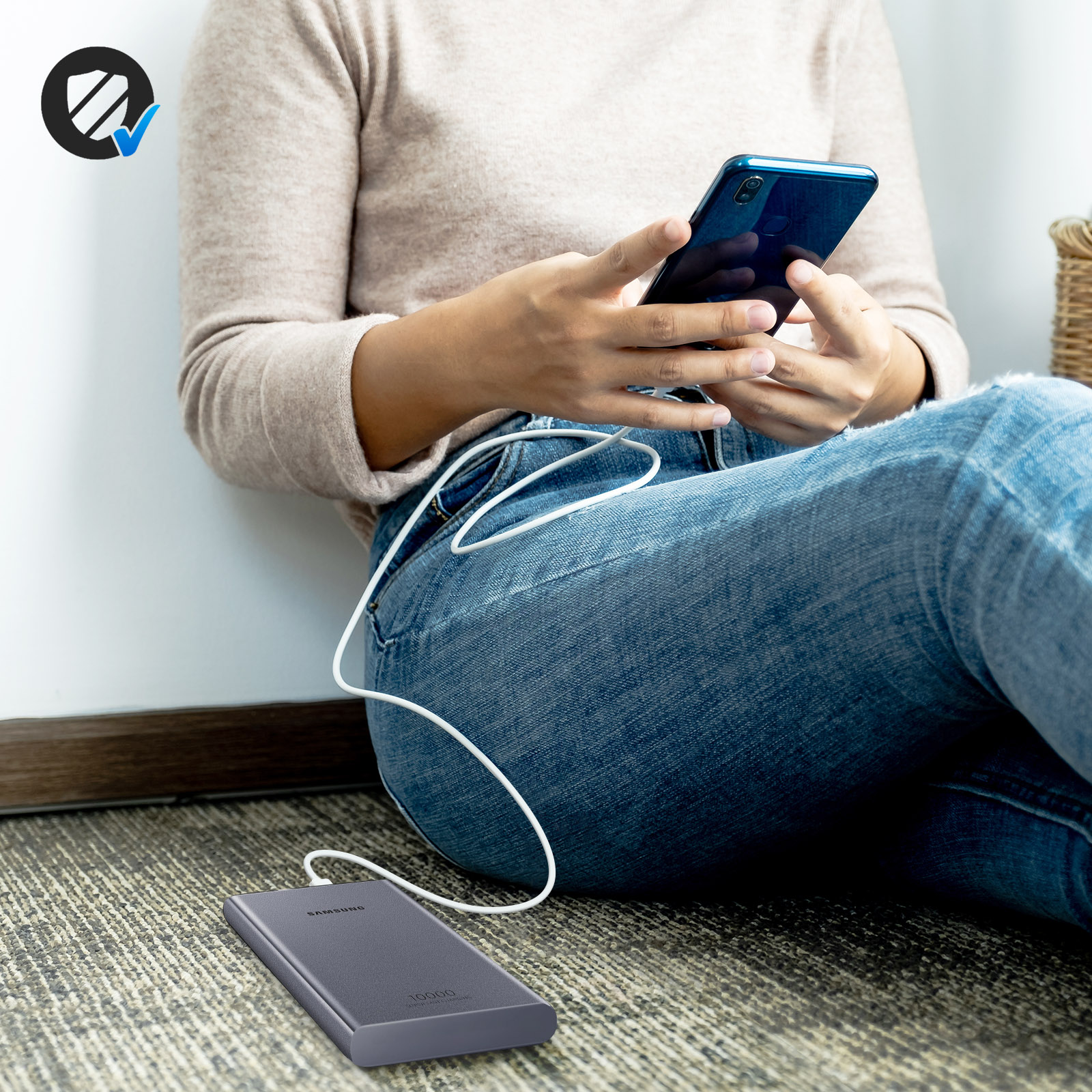 Personne utilisant un téléphone bleu, connecté à une batterie externe grise via un câble blanc, sur le sol.