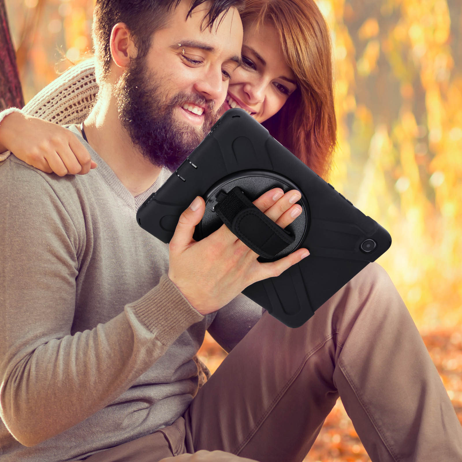 Mann und Frau halten ein schwarzes Tablet mit einem Riemen. Sie sind im Freien mit Herbstlaub.