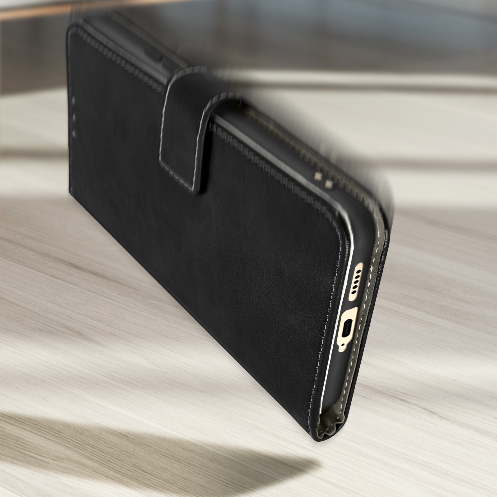 Custodia per telefono in pelle nera, leggermente aperta, su una superficie di legno chiaro. Cuciture bianche.