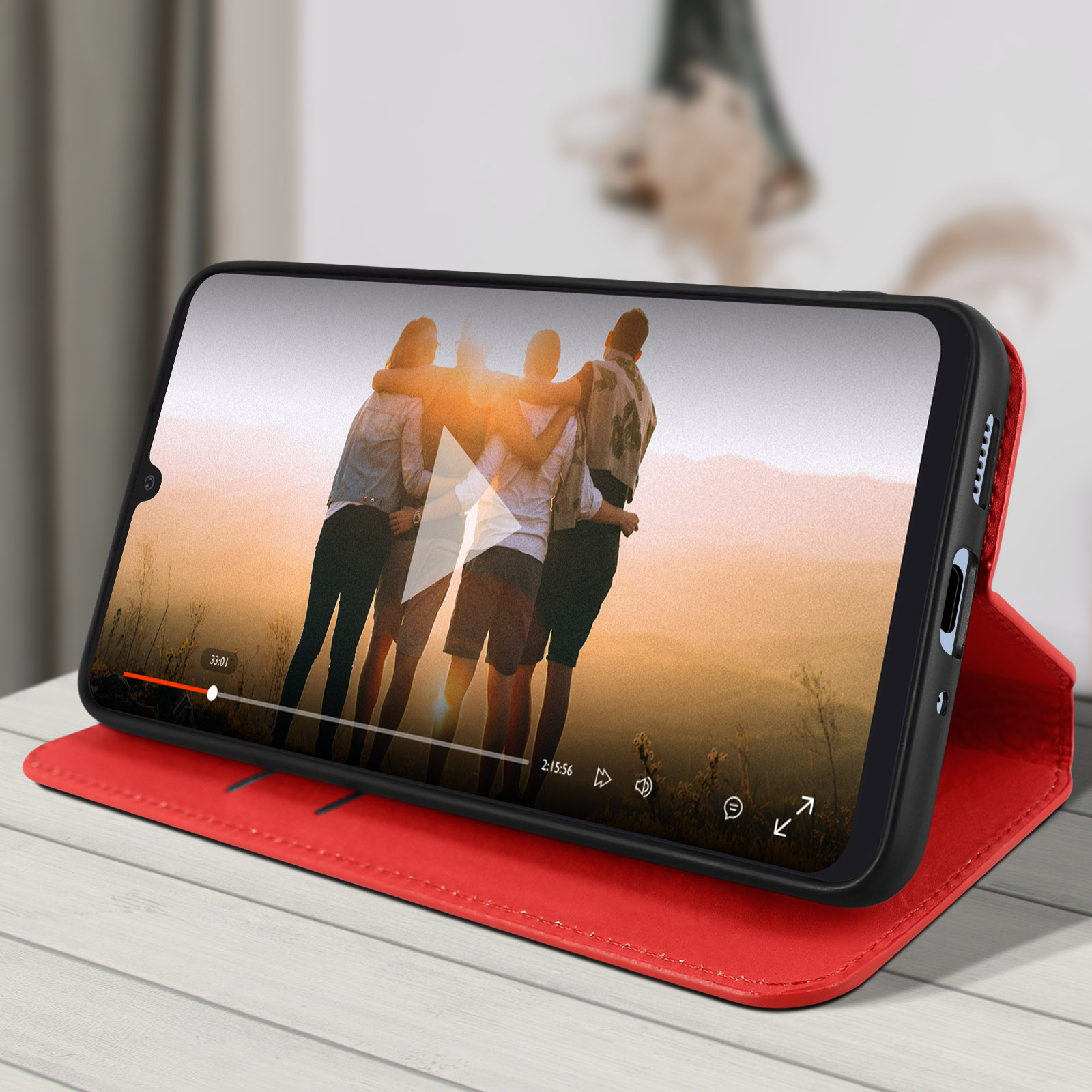 Telefoon in een rode hoes speelt video af. Mensen omhelzen elkaar, de scène is bij zonsondergang.