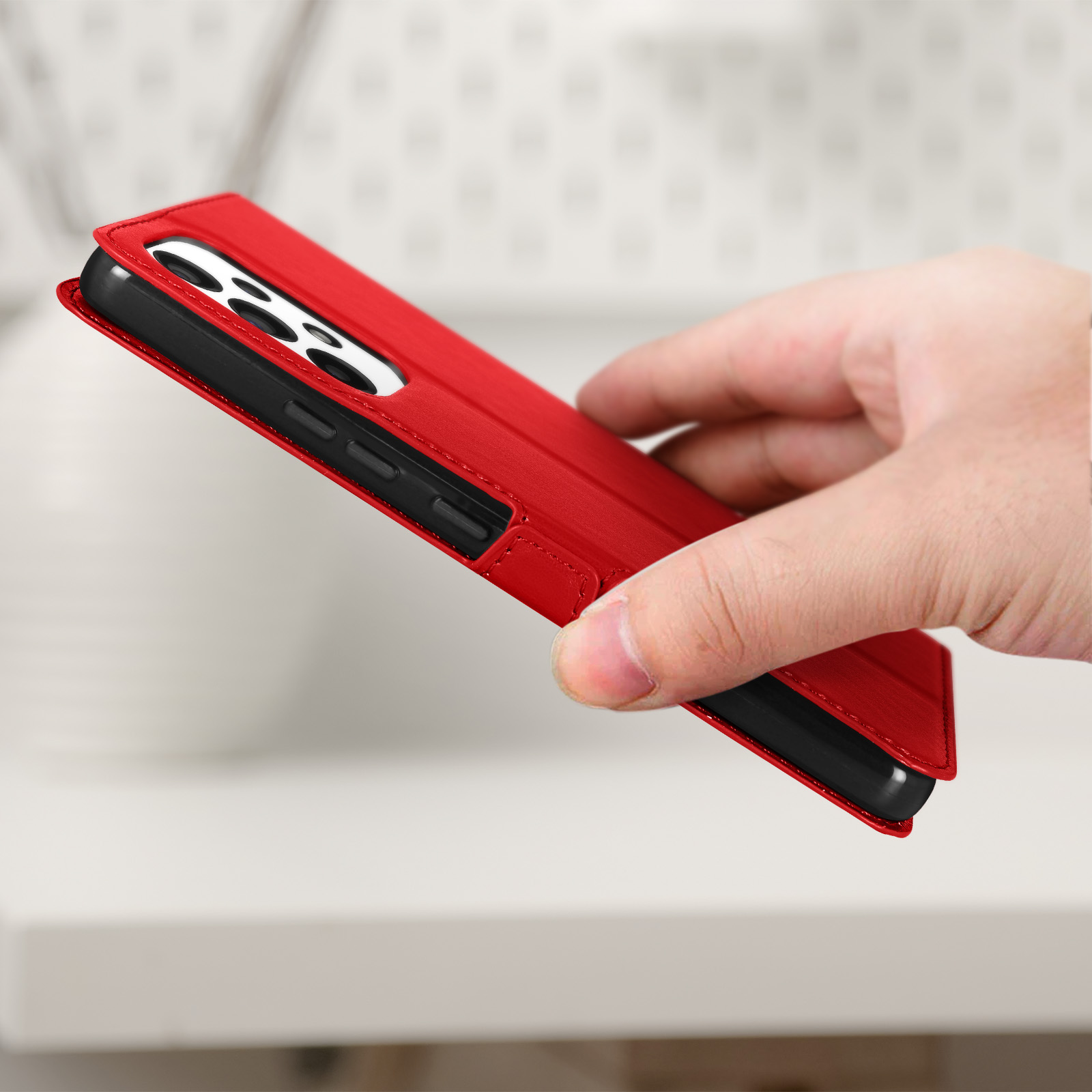 Coque de téléphone rouge tenue par la main, sur une surface blanche. Le téléphone est dedans.
