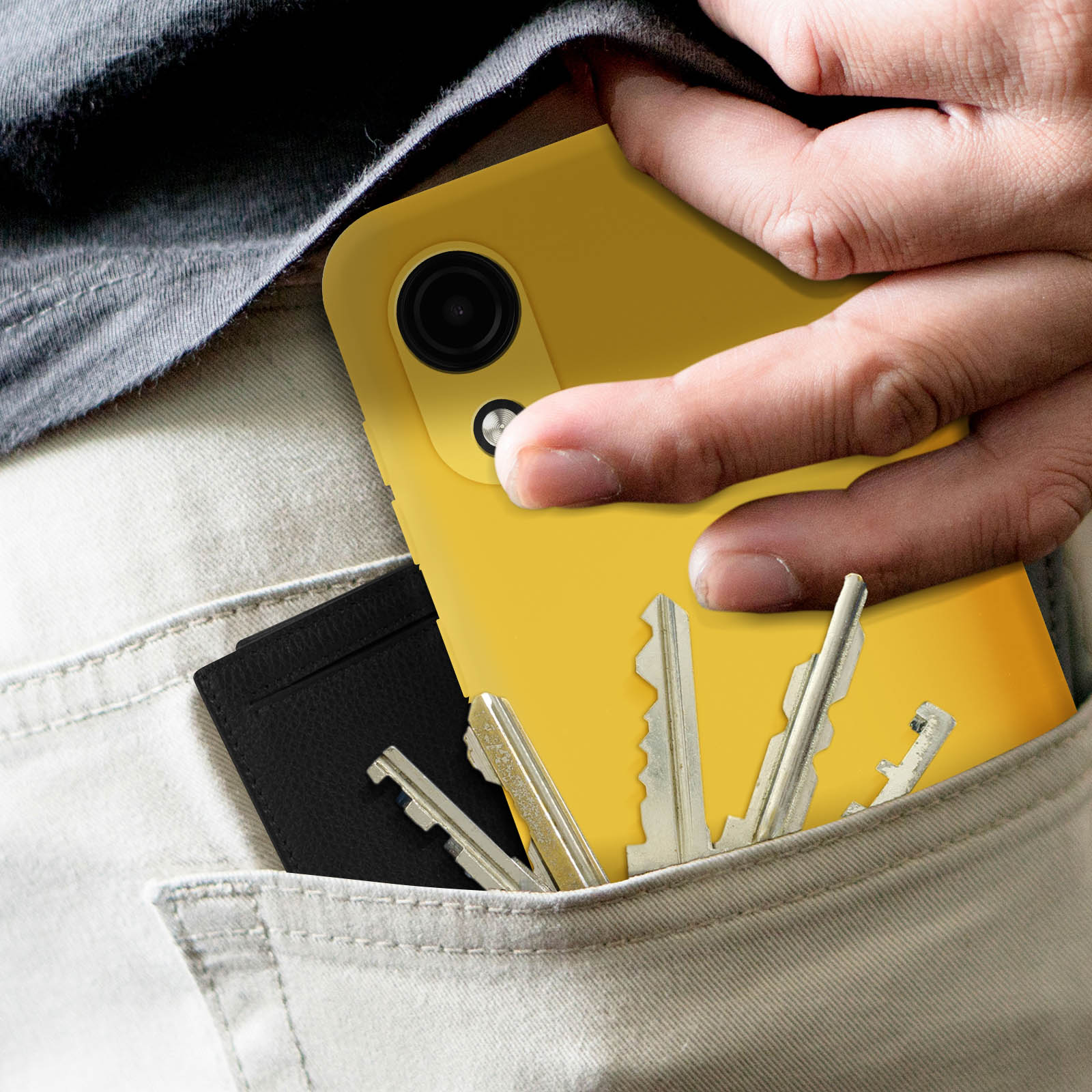 Mano con telefono giallo in tasca con chiavi e portafoglio. Pantaloni chiari.