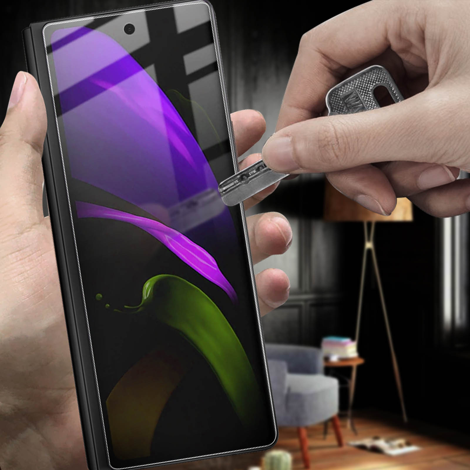 Mano che tiene un telefono con schermo viola e verde, chiave che lo graffia. Sfondo: lampada, sedia, tavolo.