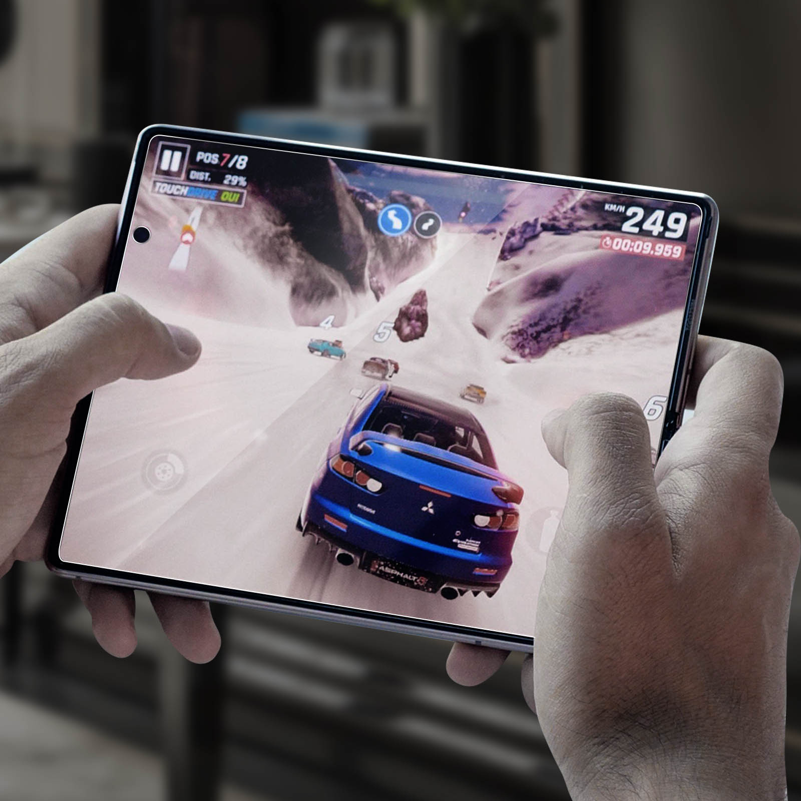Una persona tiene in mano un tablet che mostra un gioco di corse automobilistiche. Un'auto blu sfreccia su una pista innevata. L'interfaccia del gioco è visibile.