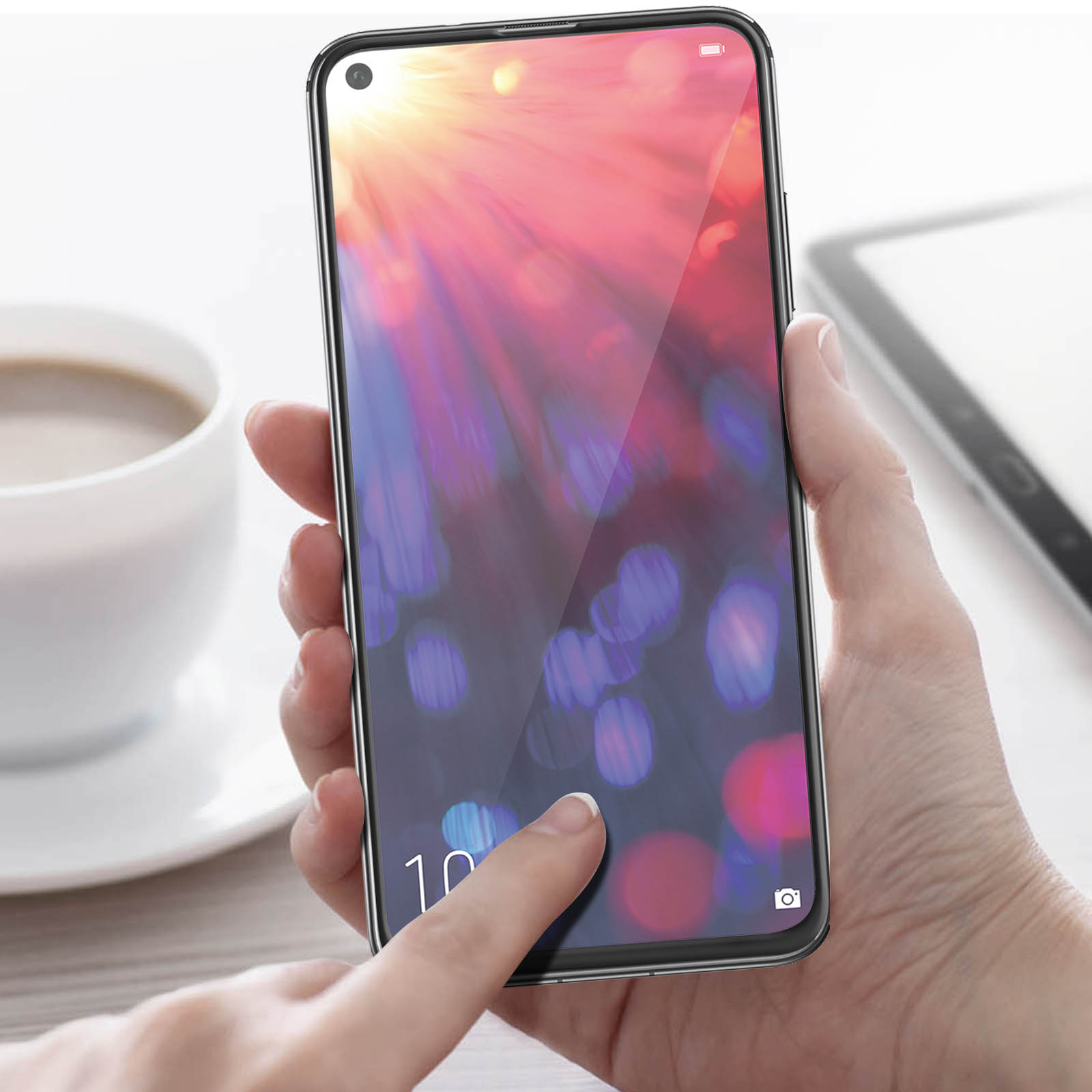 Una mano tocca lo schermo di un telefono che mostra bokeh colorato. Una tazza e un tablet sono sullo sfondo.