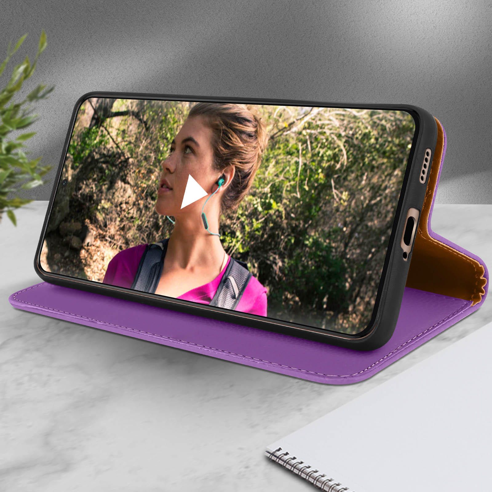 Un telefono in una custodia viola, che mostra una donna con le cuffie. La custodia è aperta, su un tavolo.