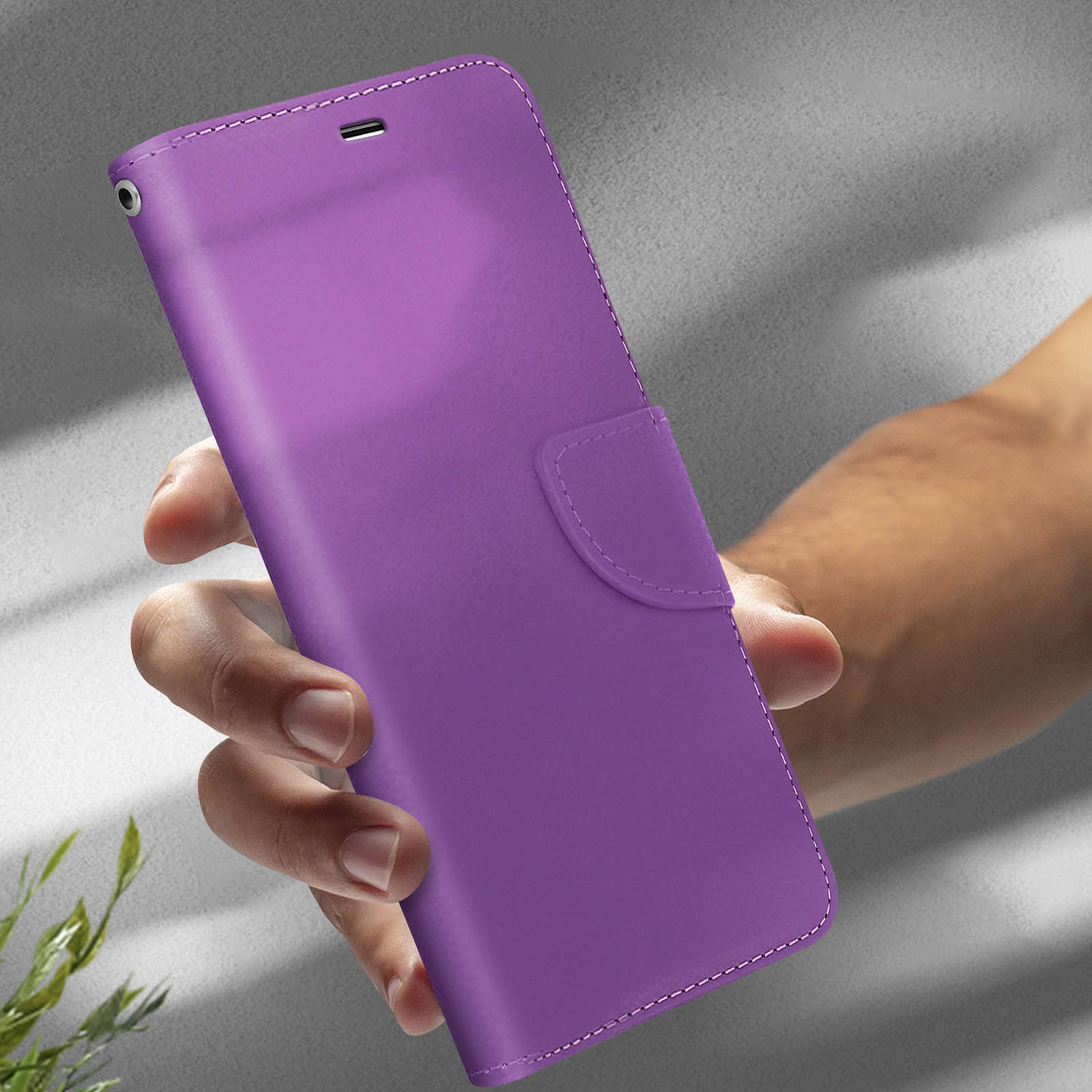Custodia per telefono viola tenuta in mano. La custodia ha una patta e una chiusura a bottone. Sfondo chiaro.