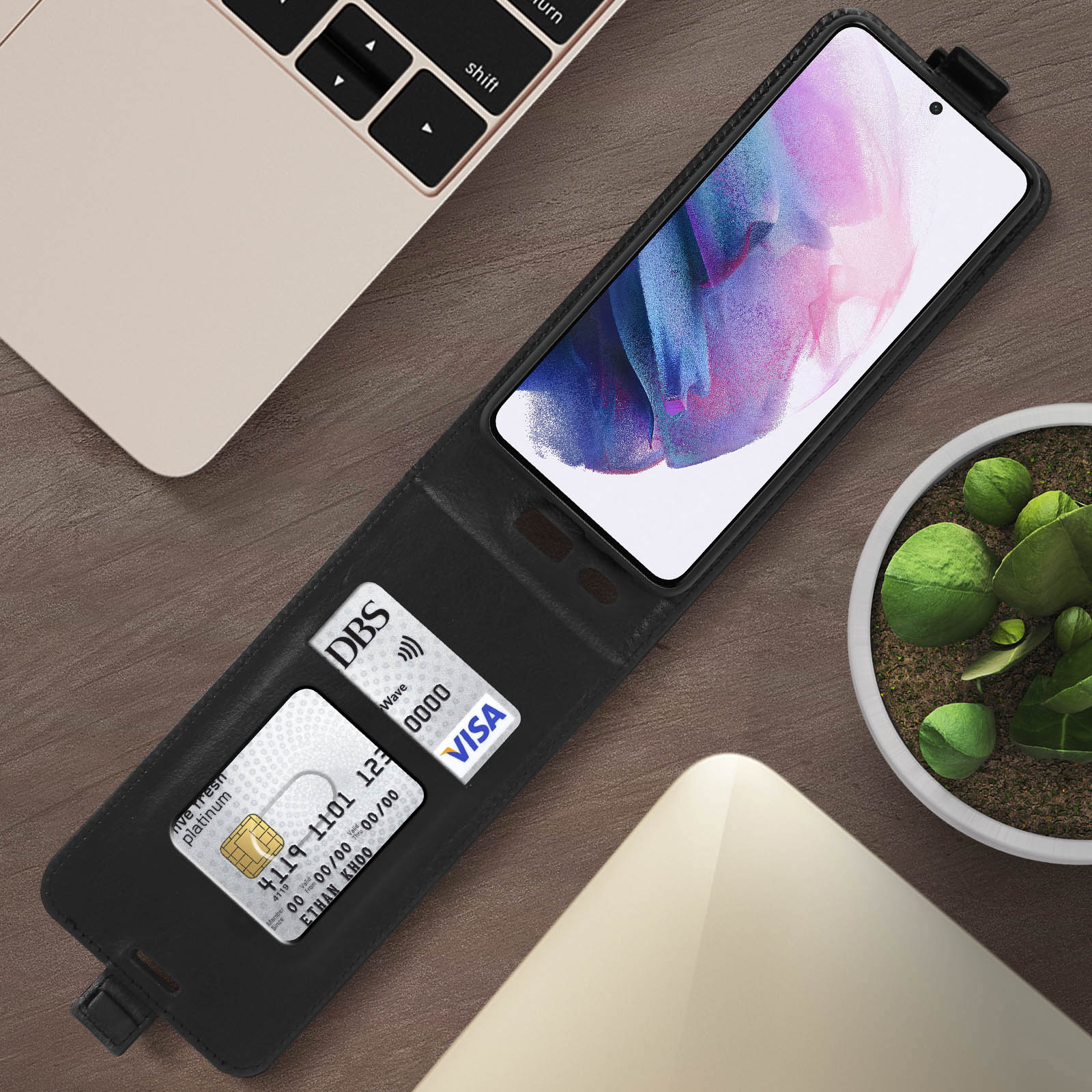 Custodia telefono nera aperta, mostra telefono. Carte e laptop sullo sfondo.