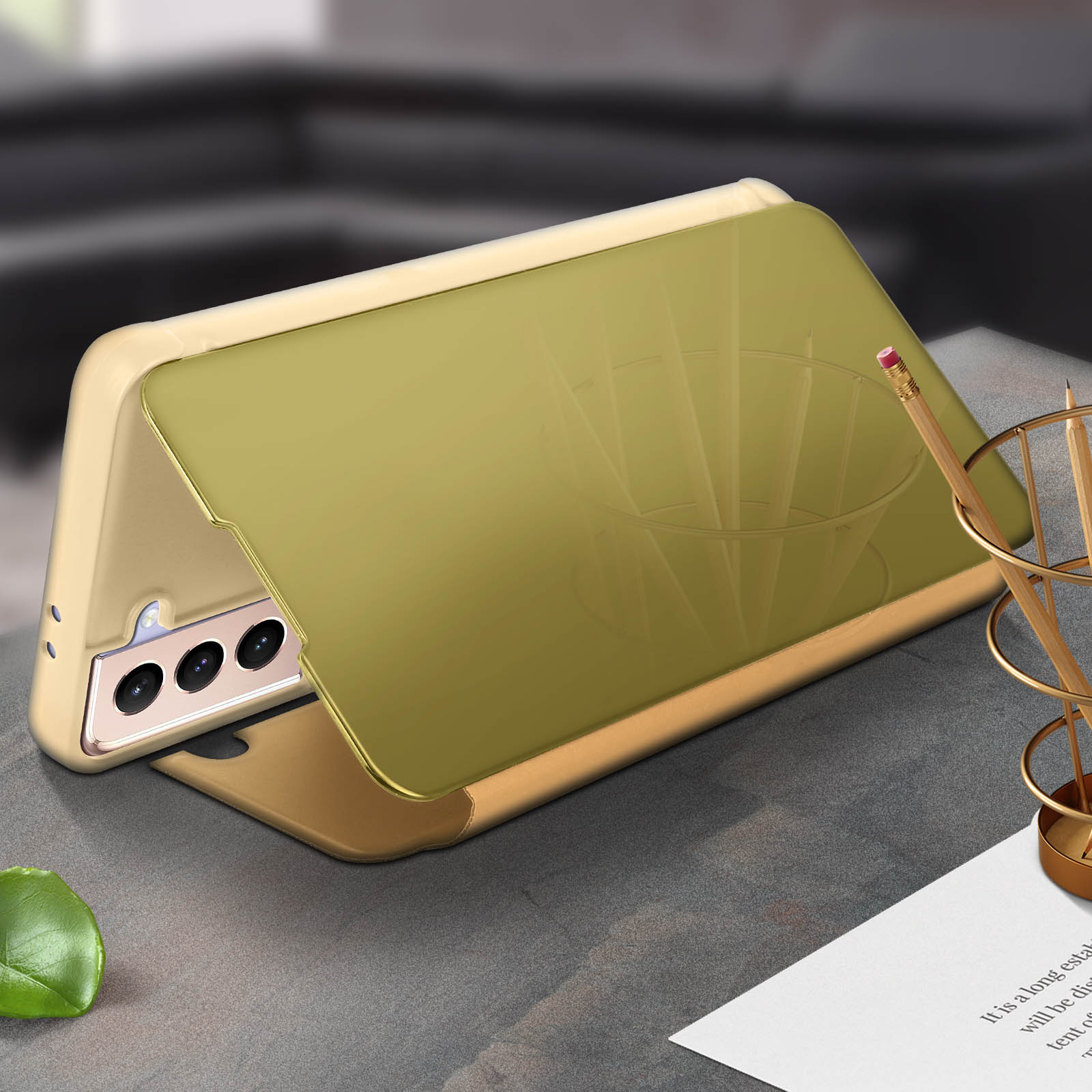 Telefoon in een beige hoes, met een gouden spiegelklep open. Potlood en decoratie op de achtergrond.