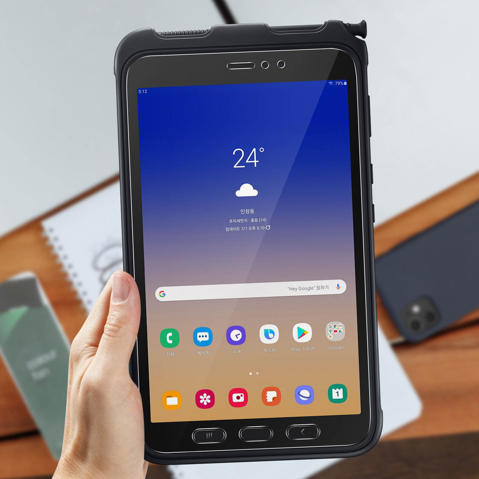 Un tablet nero in una custodia nera. Una mano lo tiene, lo schermo mostra le icone delle app e l'ora.